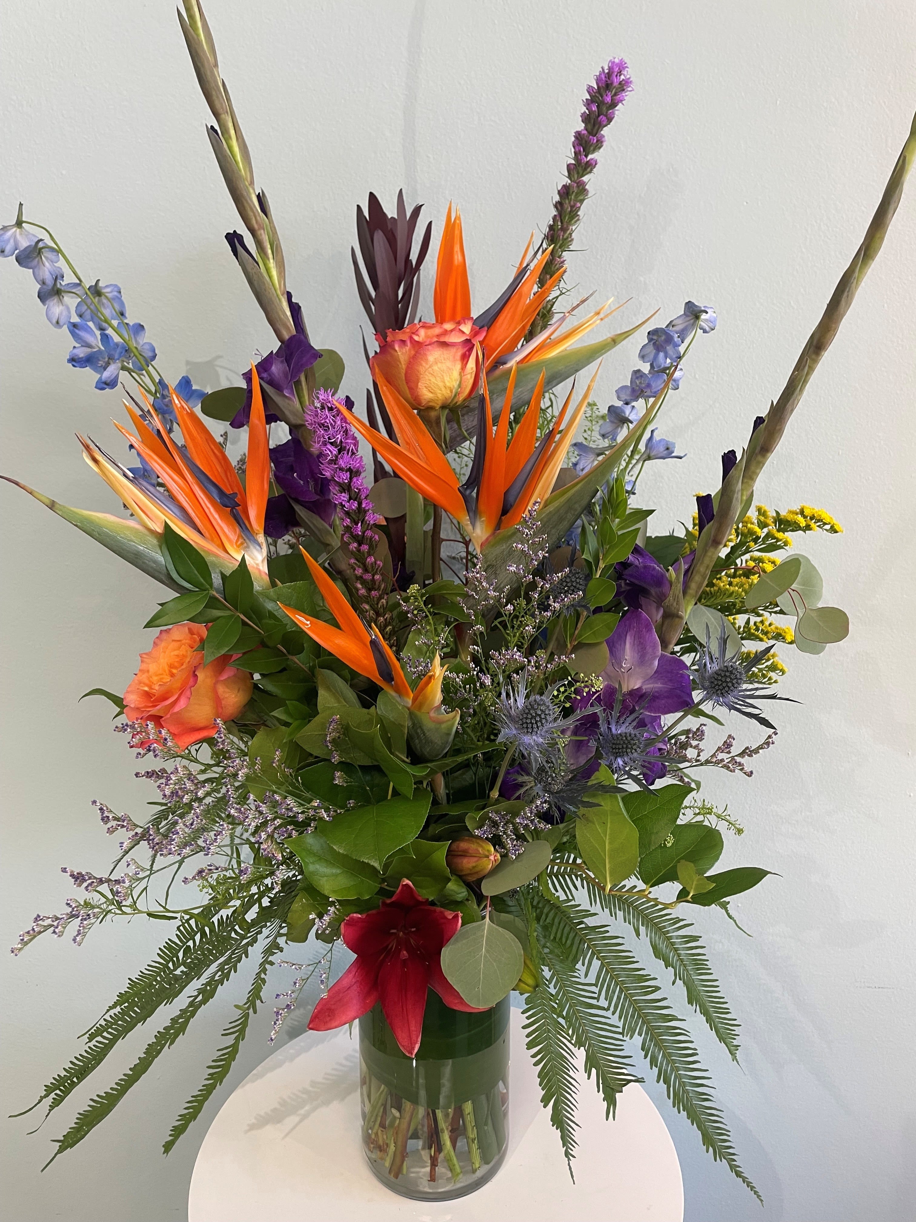 $200 Luxury Tropical Designer's Choice - Starting at $200, this luxury tropical arrangement will include our best tropical florals that we have in stock. This large arrangement is perfect for any tropical flower super fan. If your recipient enjoys the beach or tropical vacations, this makes the perfect gift. This arrangement may include flowers such as birds of paradise, leucadendron, palm assortments, lilies, delphinium, and other bright tropical flowers and greenery.  *The arrangement pictured is an example of what we do for the price and gives the general idea of the size and style. This arrangement will not be replicated unless requested (we would need a week's notice to insure freshness). The arrangement is labeled as "Designer's Choice" meaning we will utilize what we have available and of best quality at the time.