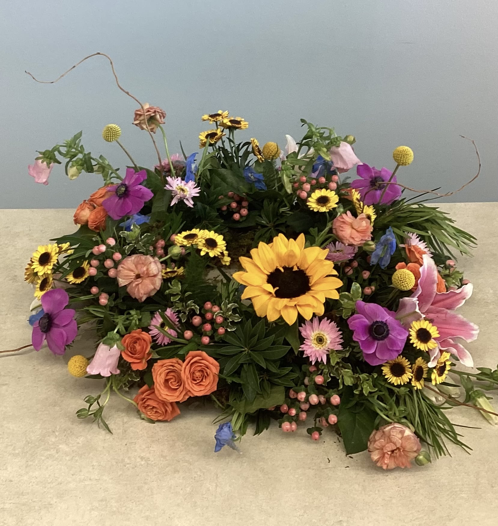 Sympathy Urn Wreath - Bright mixed blooms in yellow, pink, orange, and purple-sunflower-centered, with roses, daisies and carnations-an abundant, cheerful urn wreath offering warm, uplifting sympathy.