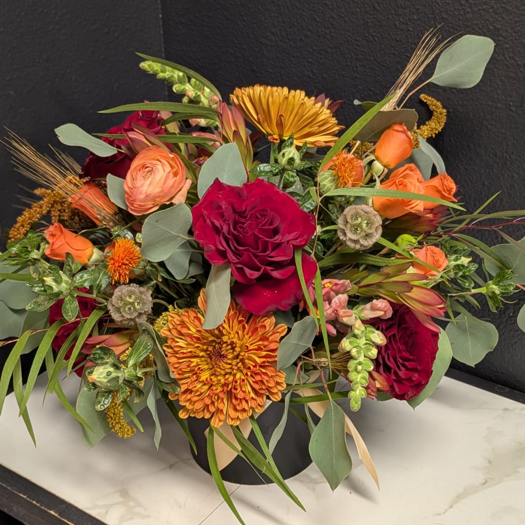 Mixed bouquet of red, orange, and peach flowers in a black vase