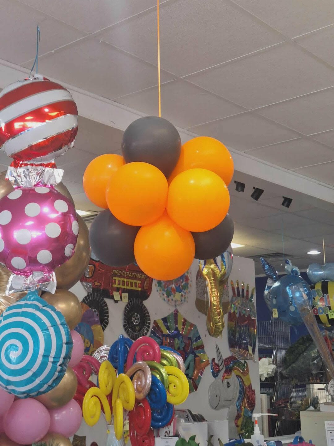 Clusters of colorful balloons hanging indoors, including orange, gray, and patterned foil balloons.