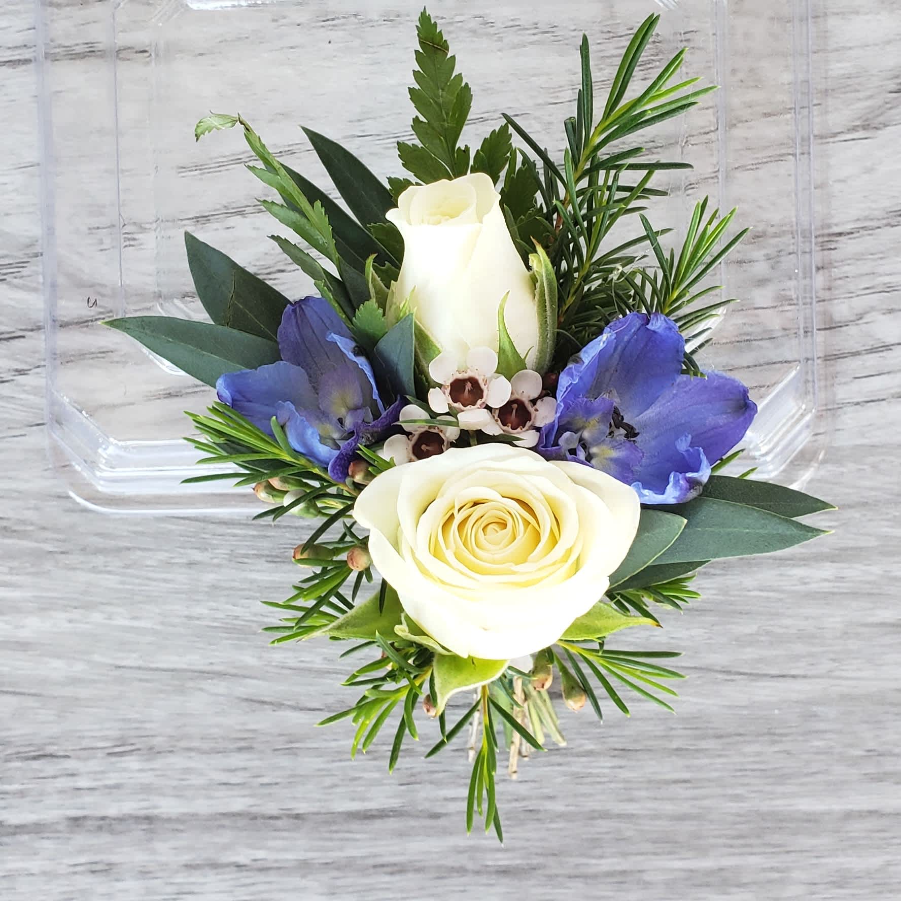 White rose boutonniere with blue flowers and greenery