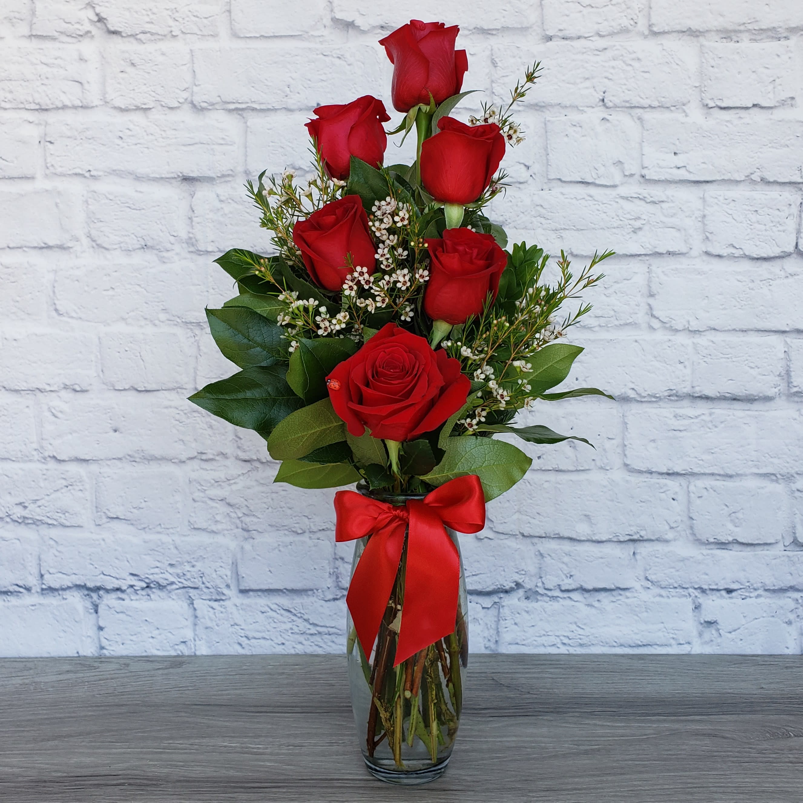 Red roses arranged in a clear glass vase with a red ribbon