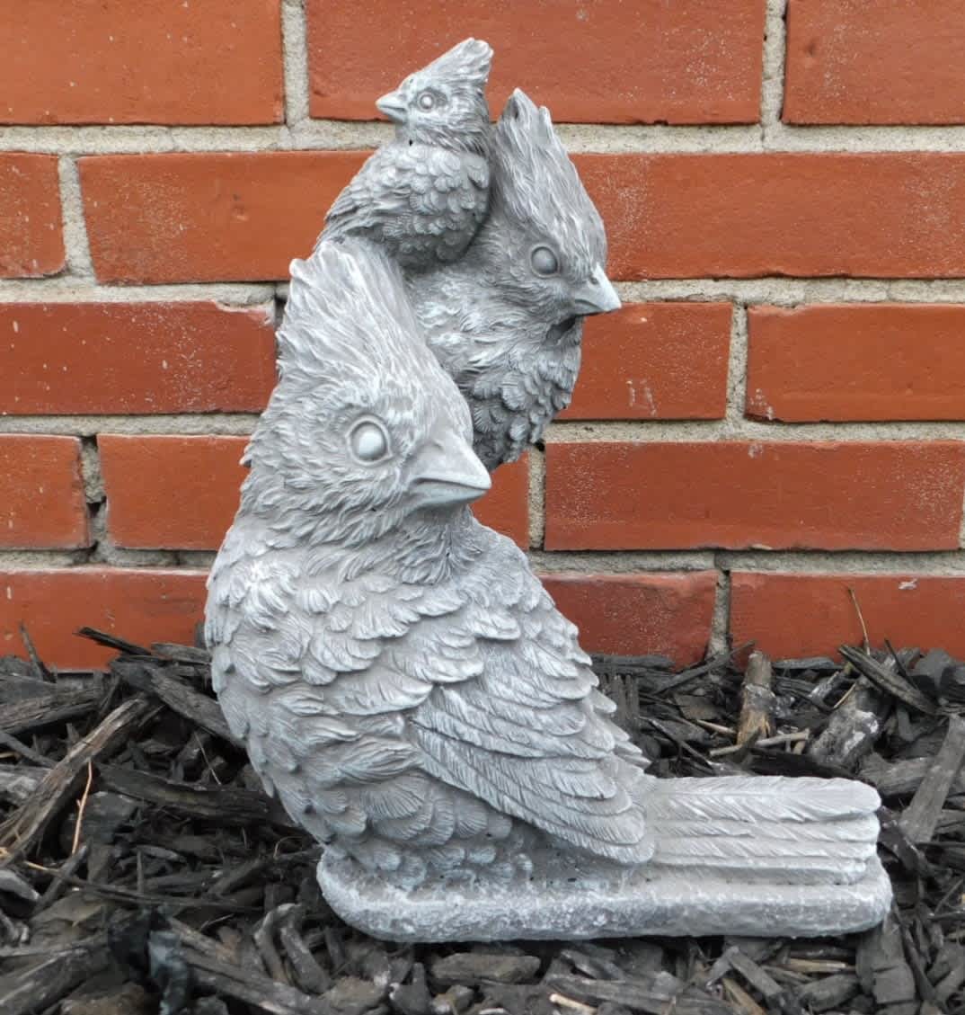 Three gray bird statues on mulch in front of a brick wall