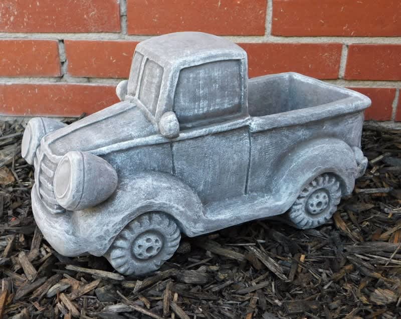 Gray pickup truck-shaped planter against a brick wall