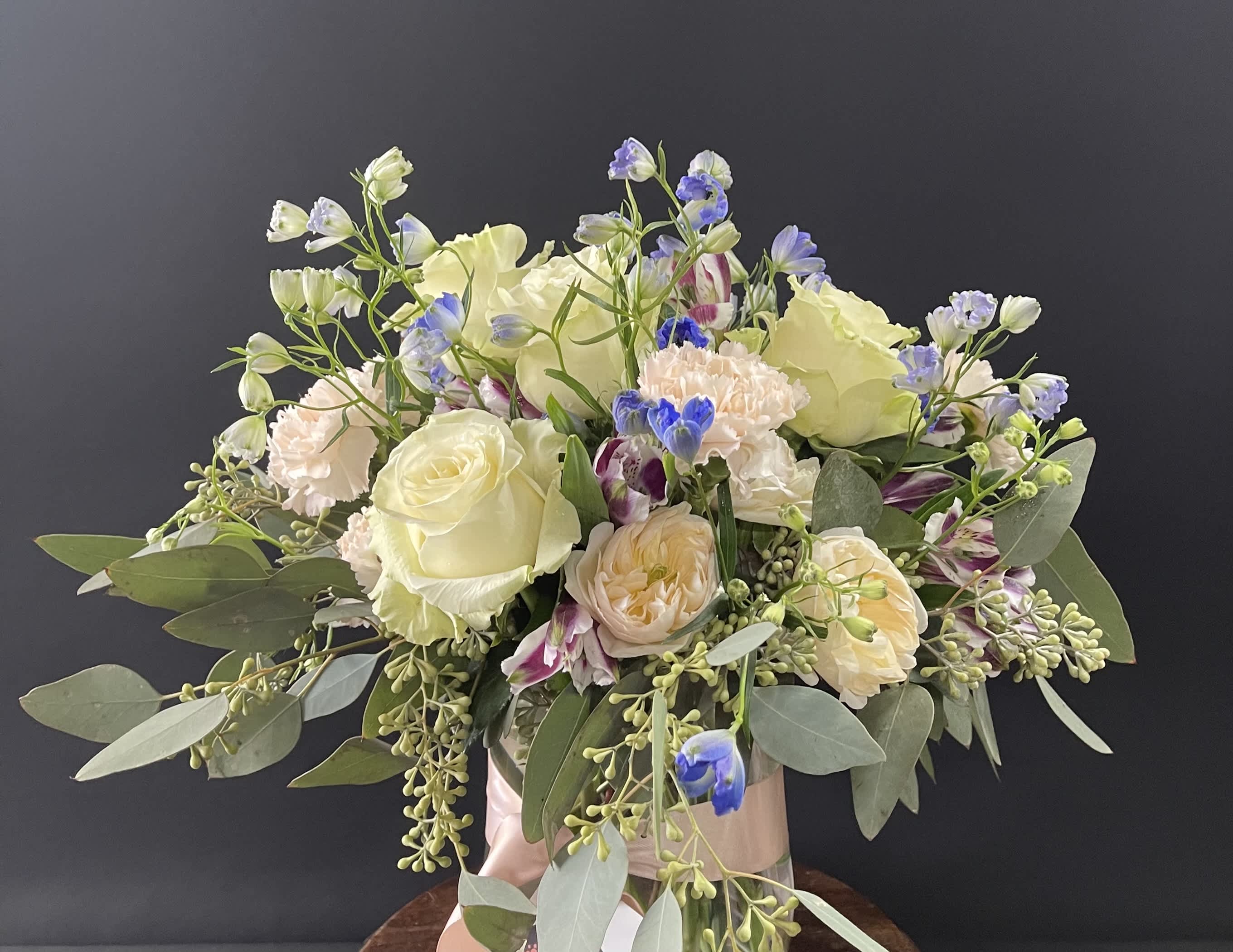 Bouquet of cream roses, pale peach blooms, and blue accents in a vase