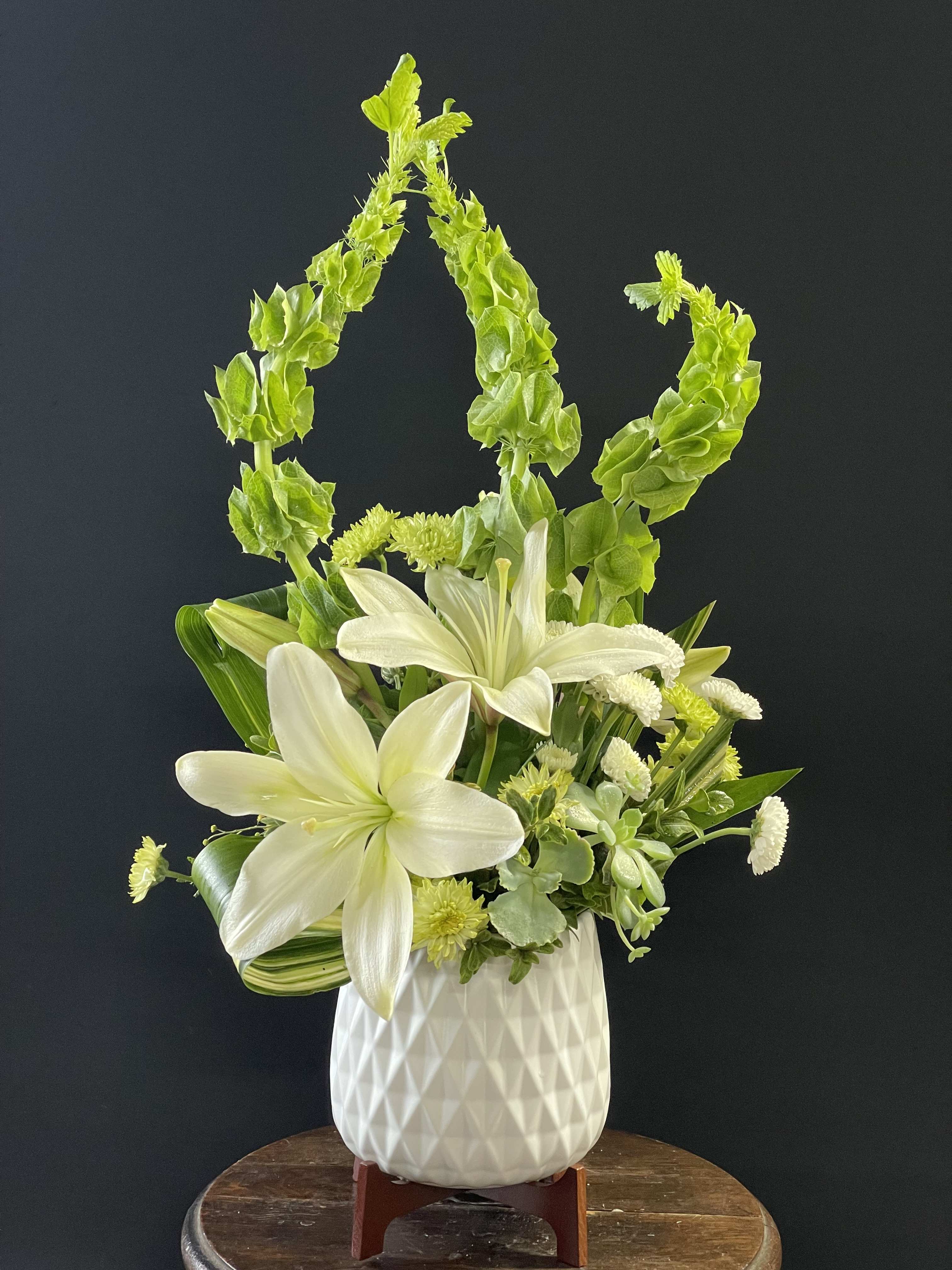 White lilies and green blooms in a white vase