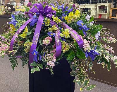 Large purple and yellow floral spray with ribbon on a stand
