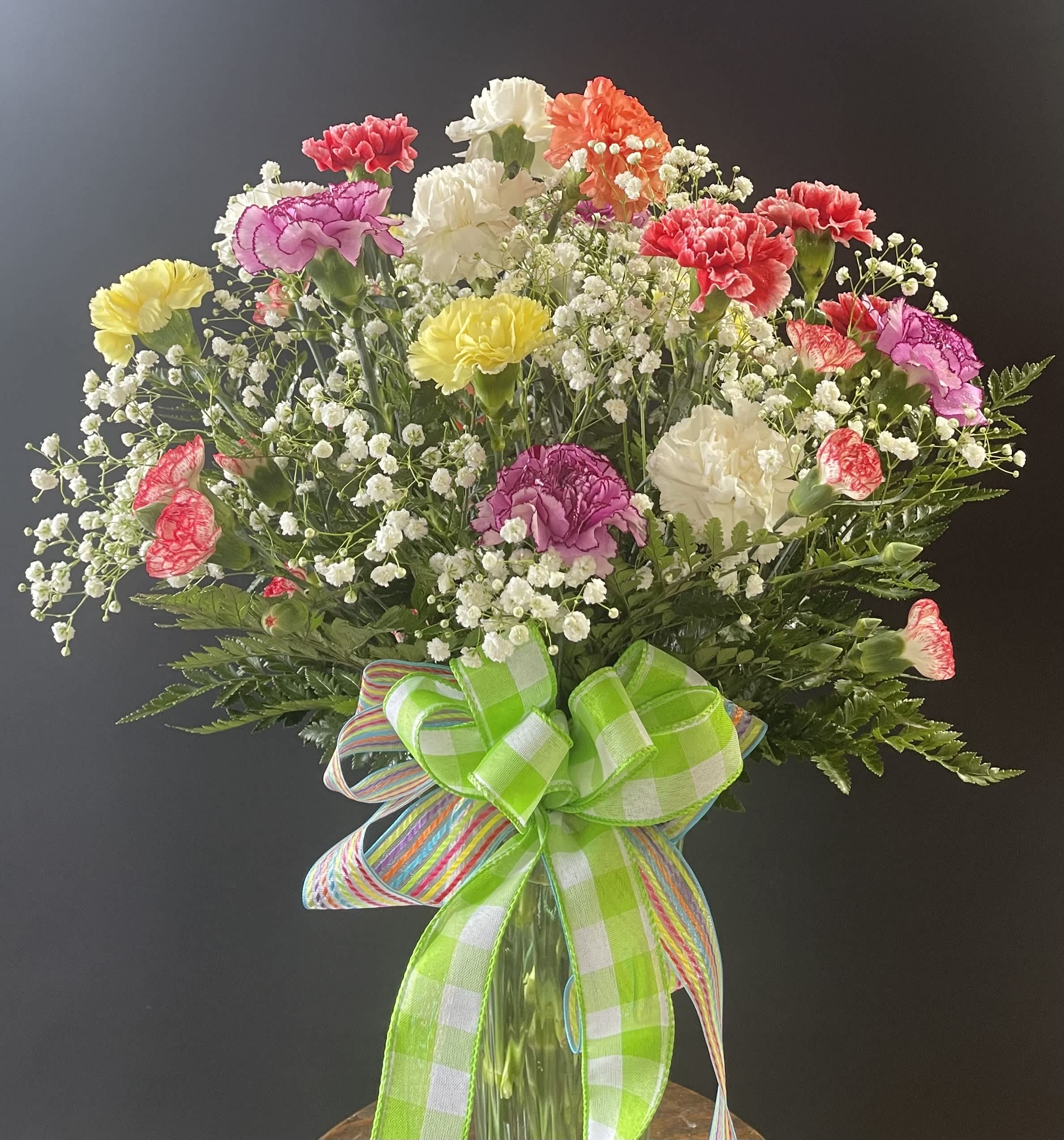 Colorful carnation bouquet in a glass vase with a large ribbon bow
