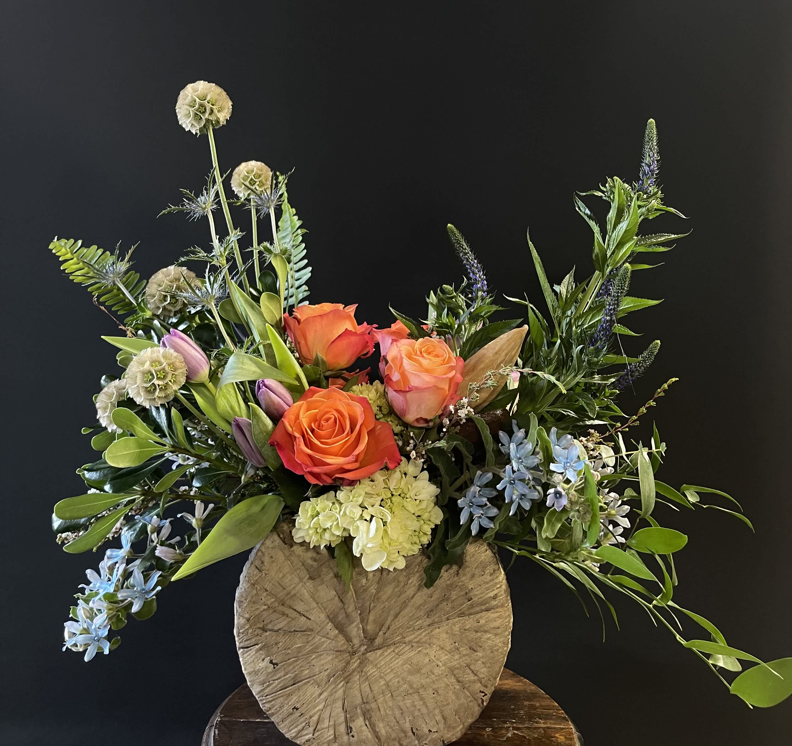 Mixed bouquet with orange roses, lilies, and blue flowers in a rustic vase