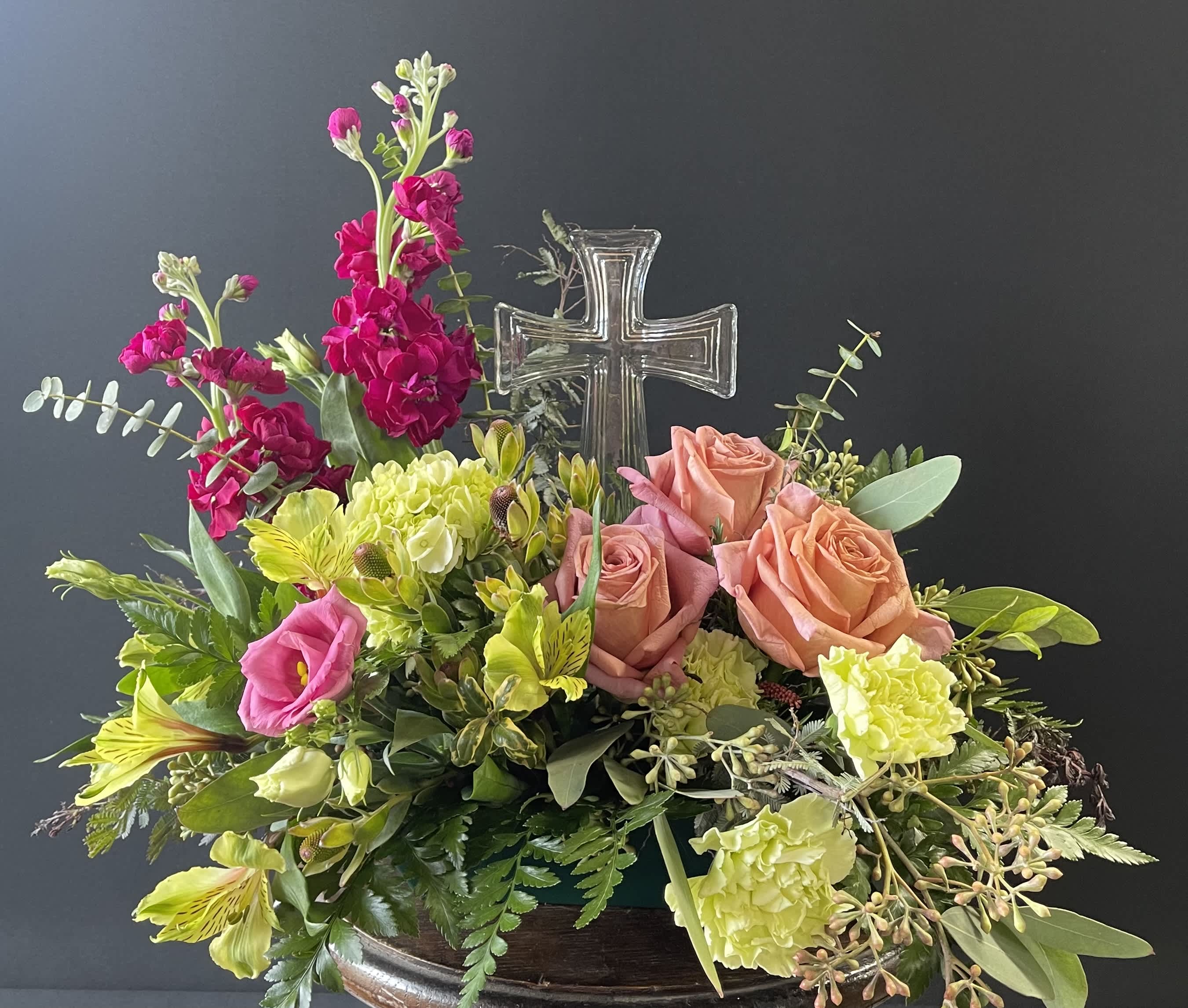 Mixed floral arrangement with roses, carnations, and a clear glass cross