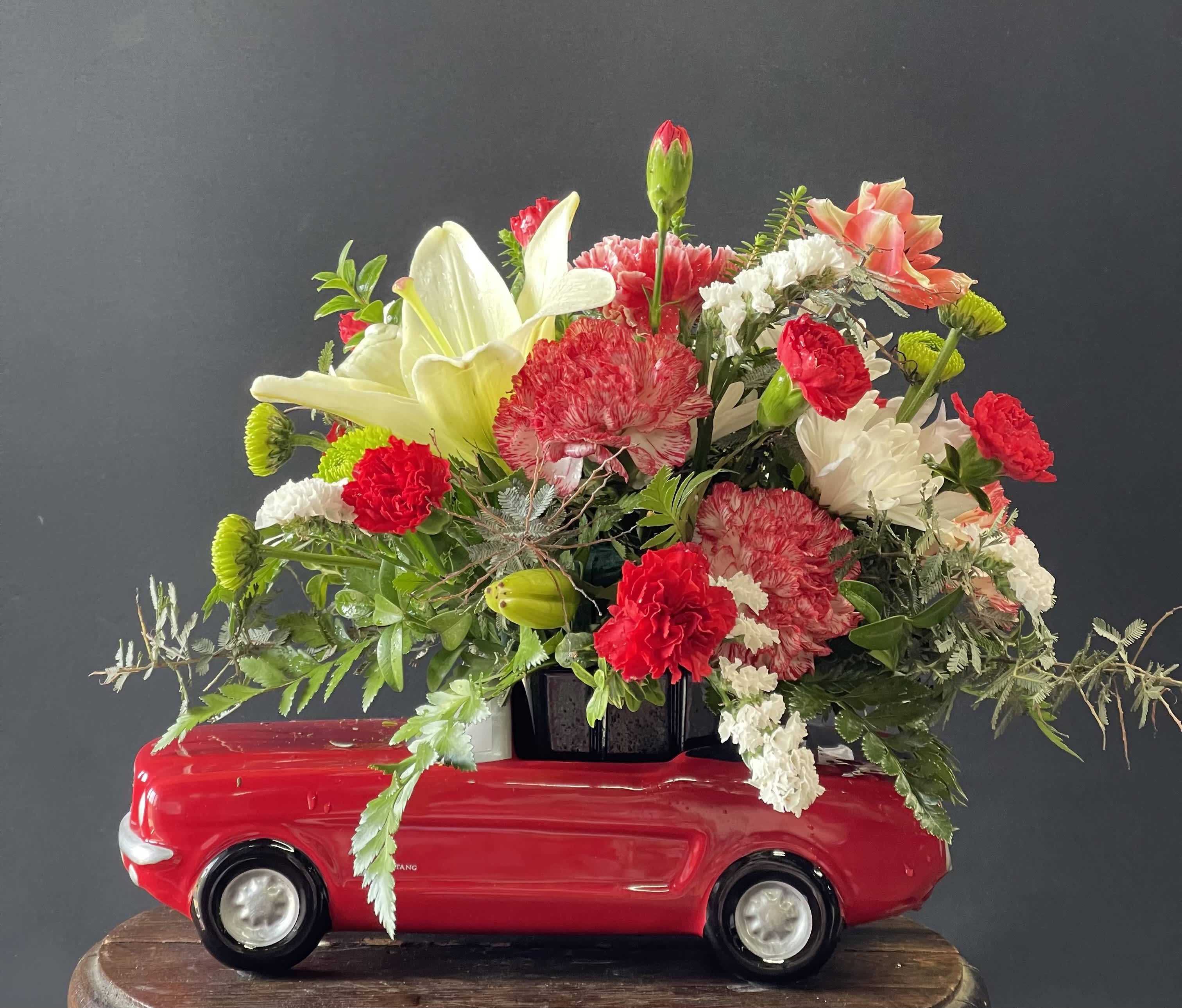 Floral arrangement in a red toy car with lilies and carnations