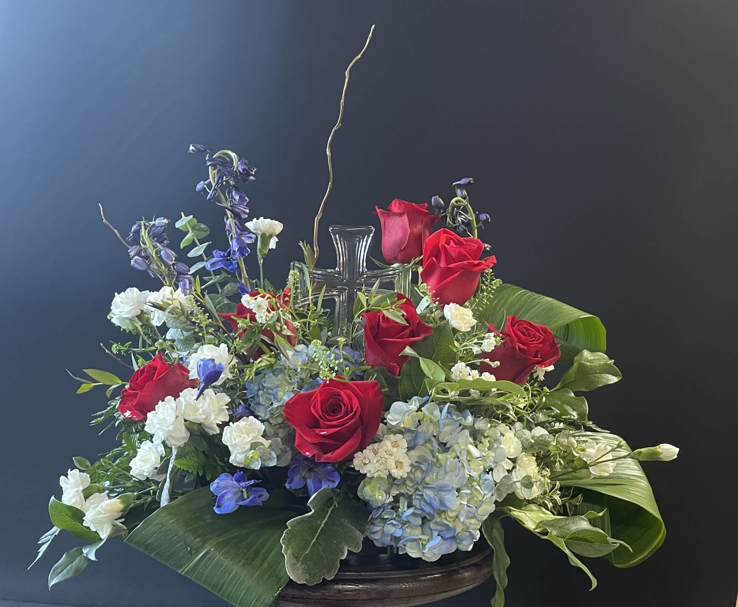 Red roses and blue-white flowers arranged around a glass cross centerpiece