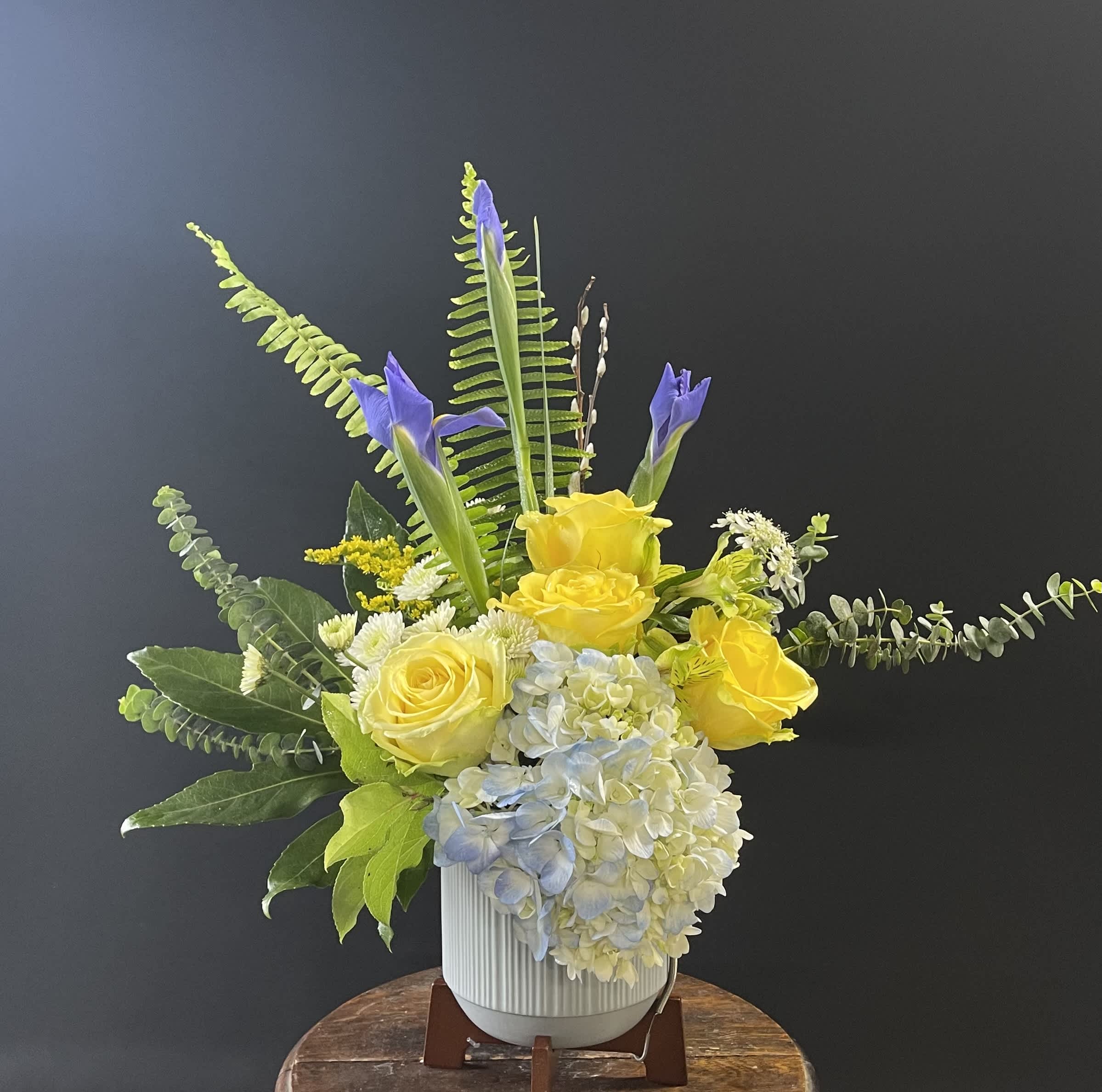 Yellow roses and blue hydrangea in a white vase with tall purple iris