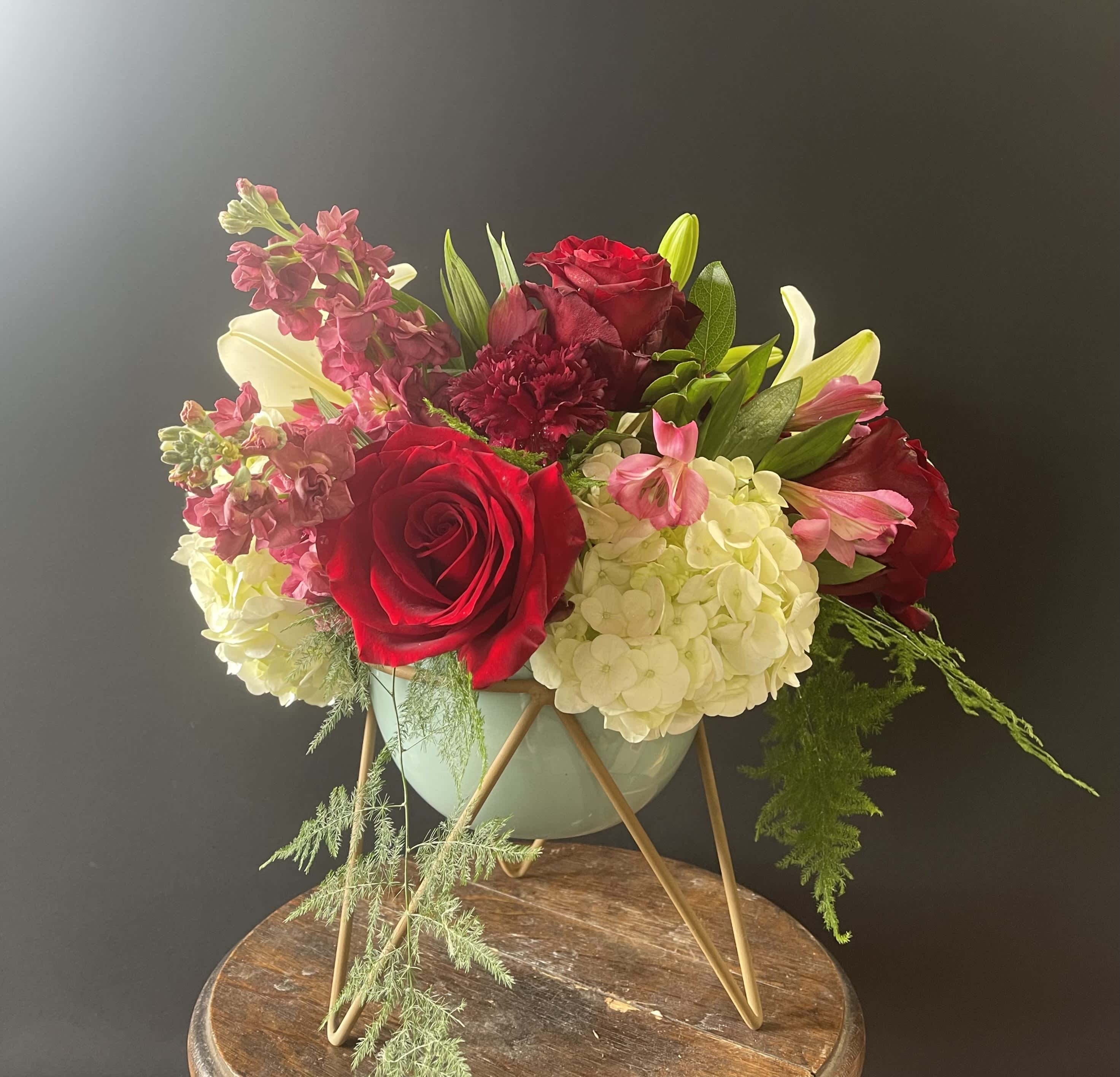 Low arrangement of red roses, white hydrangeas, and pink blooms in a mint bowl on a gold stand
