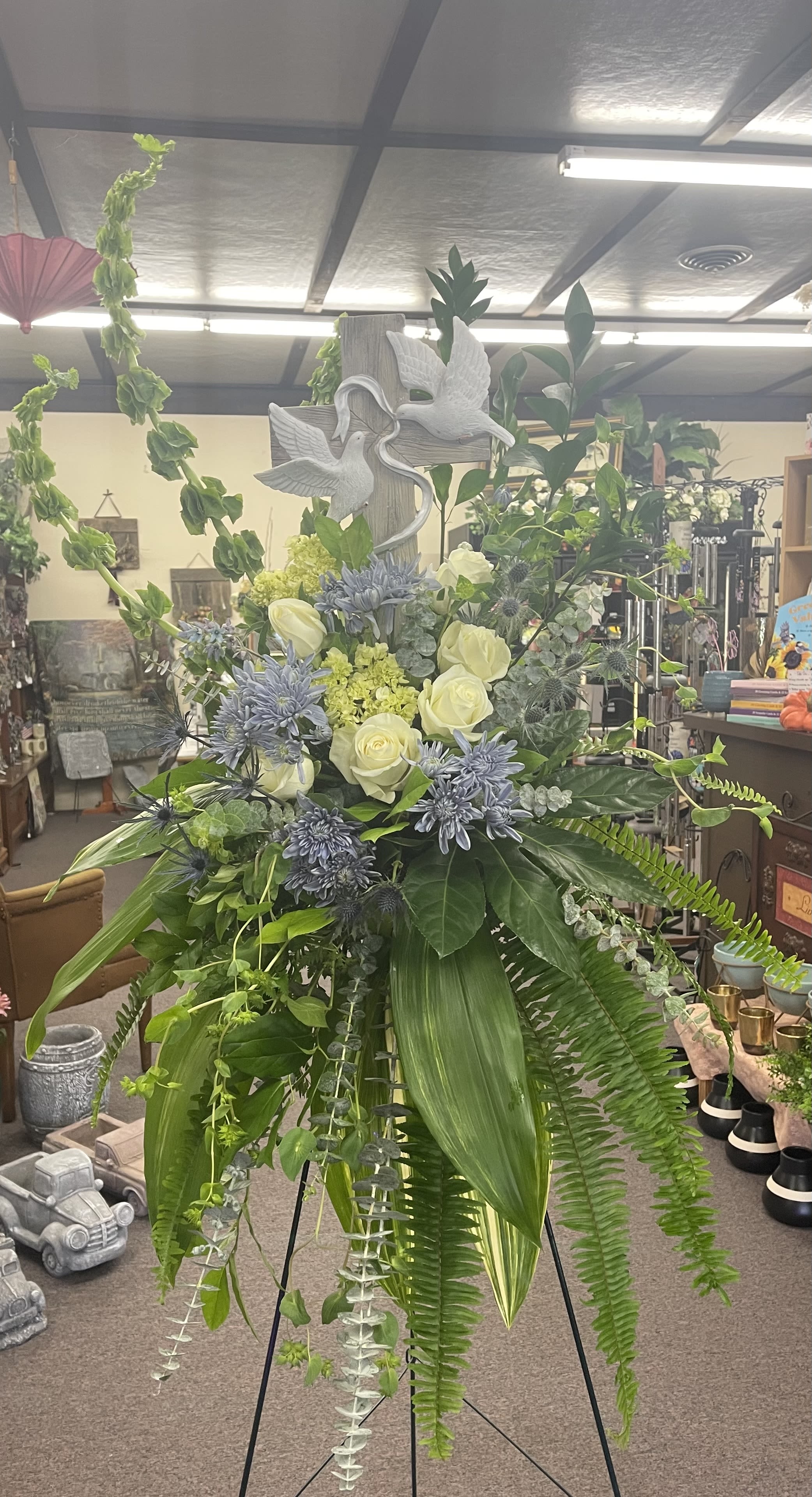 Tall floral standing spray with white roses and blue flowers on an easel