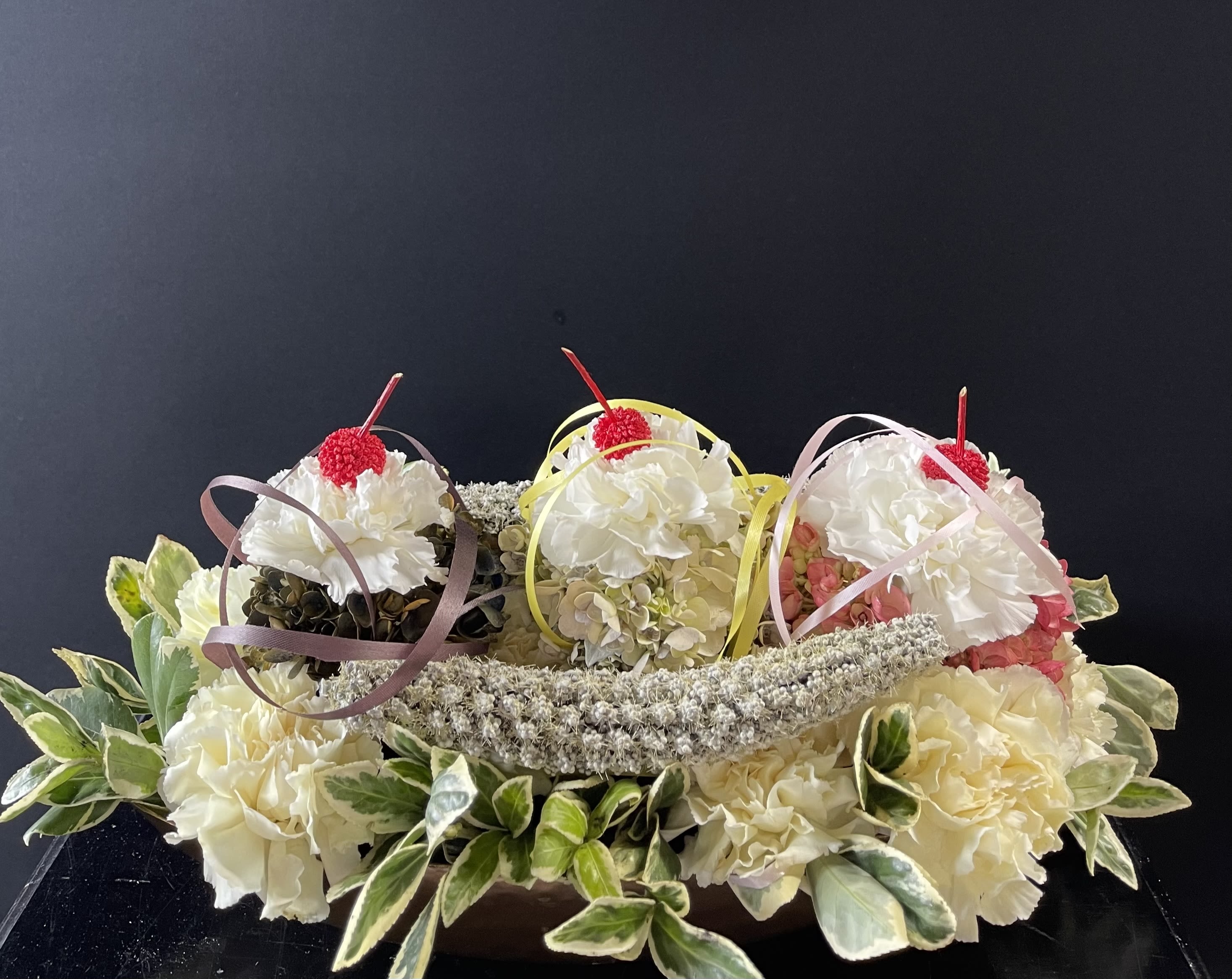 Three small floral arrangements with white blooms and ribbon loops on a dark background