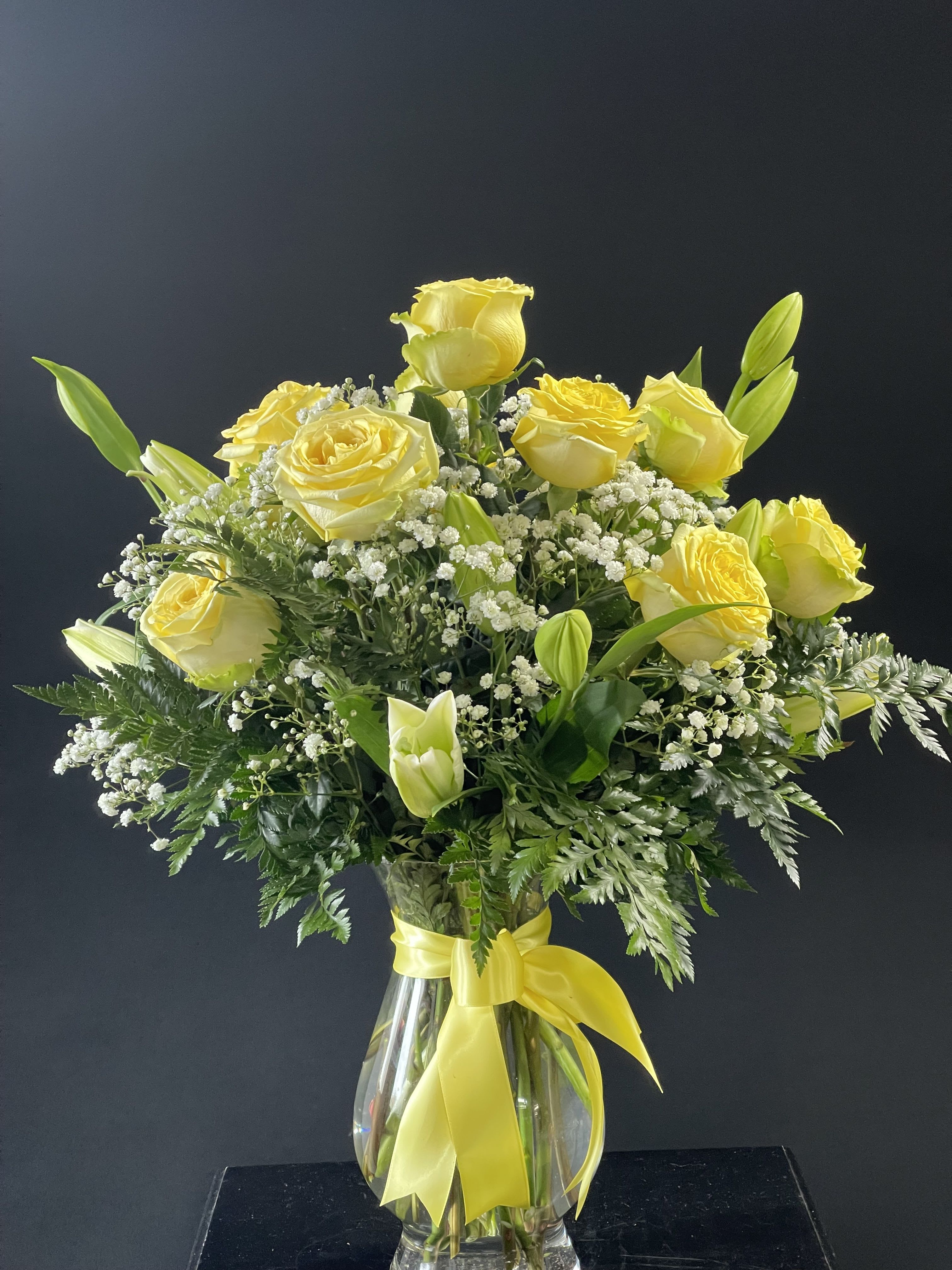 Yellow roses and lilies in a clear glass vase with a yellow ribbon