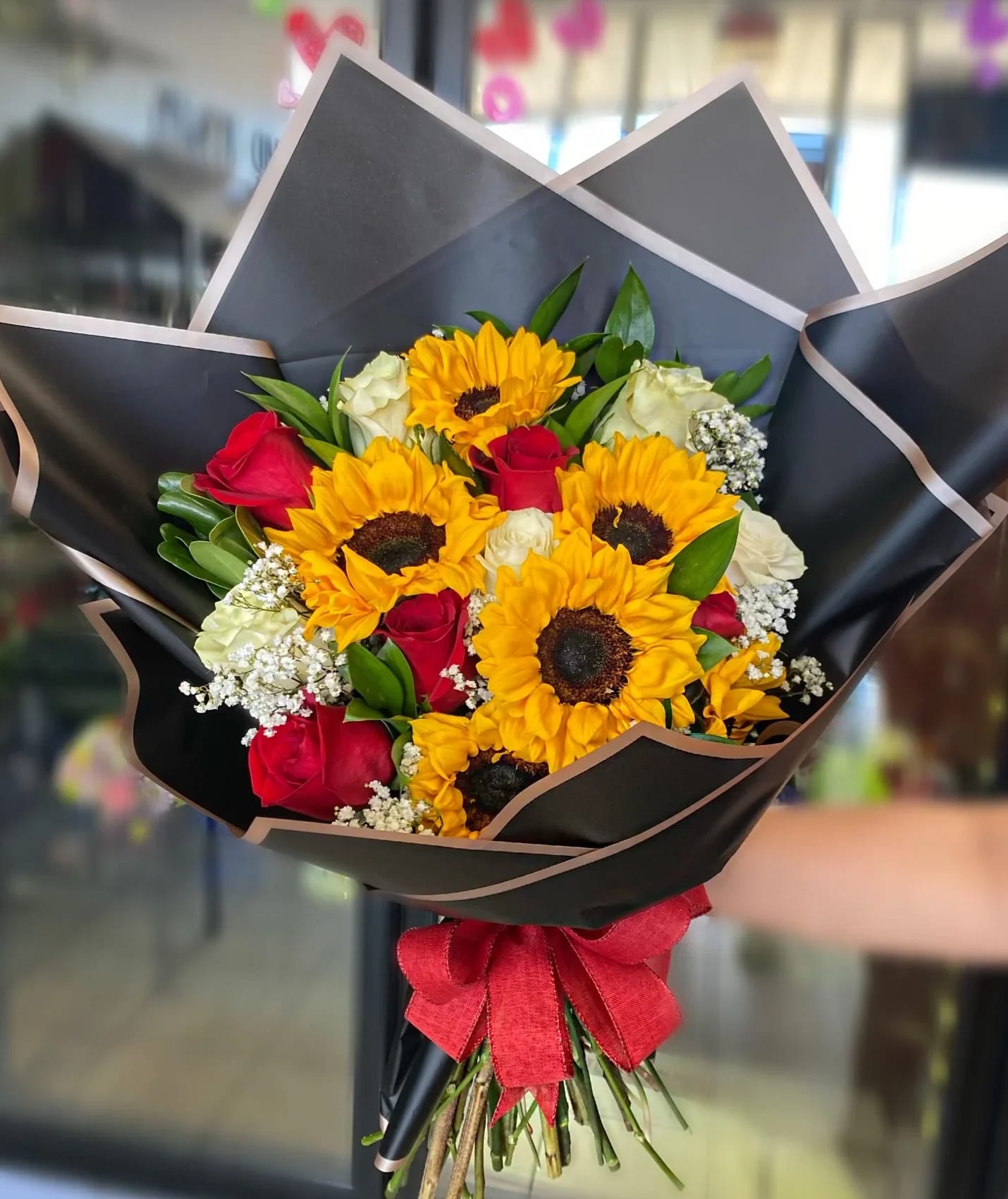 Bouquet of sunflowers and red roses wrapped in black paper with a red bow
