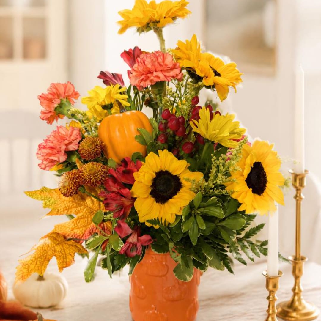 Autumn floral arrangement with sunflowers, carnations, and a small pumpkin in an orange vase