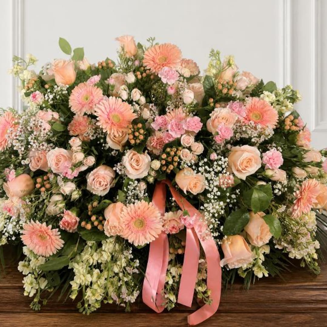 Large peach and pink floral arrangement with a pink ribbon on a wooden table