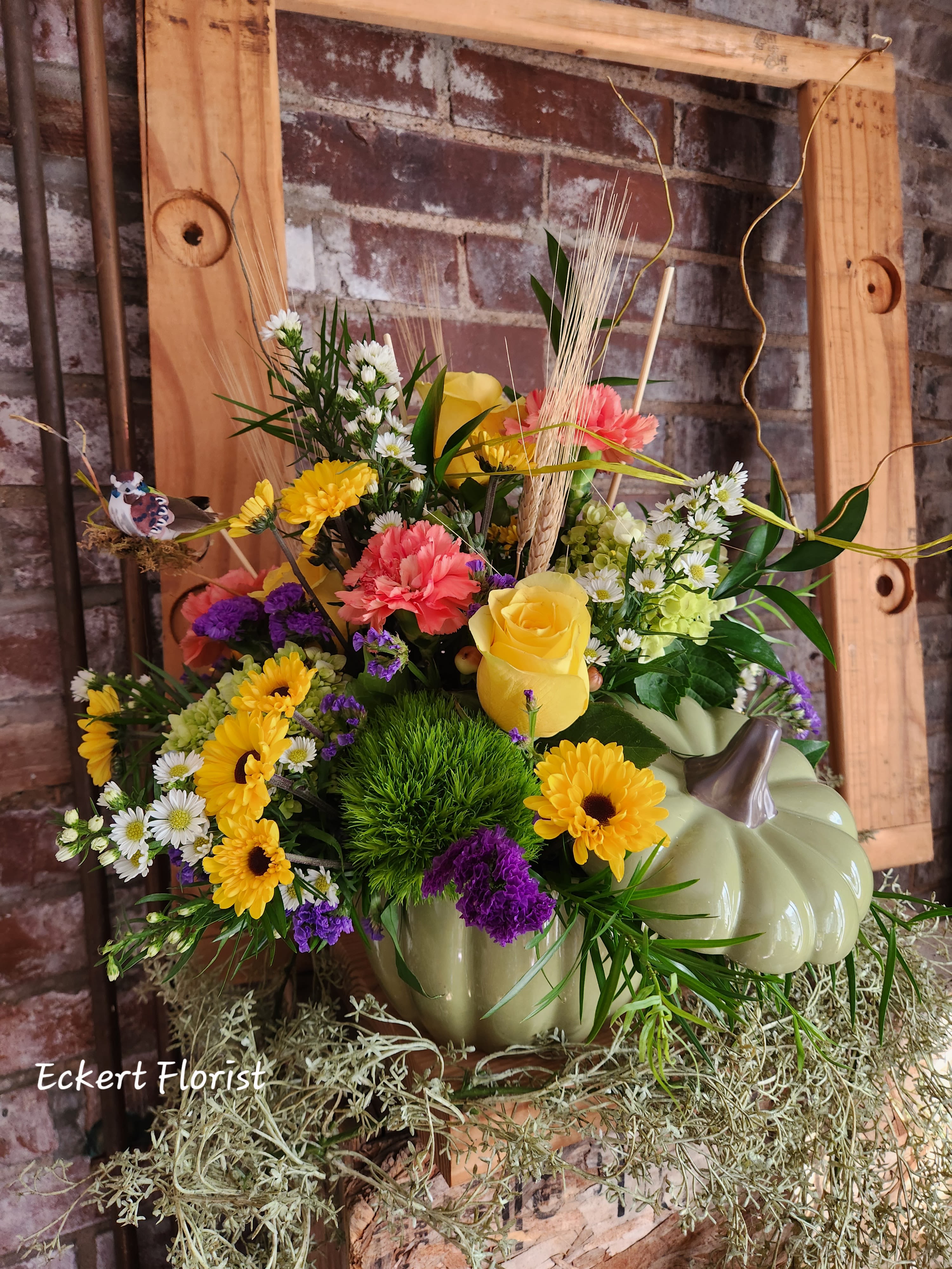Mixed flower arrangement in a pumpkin-shaped container with yellow roses and daisies