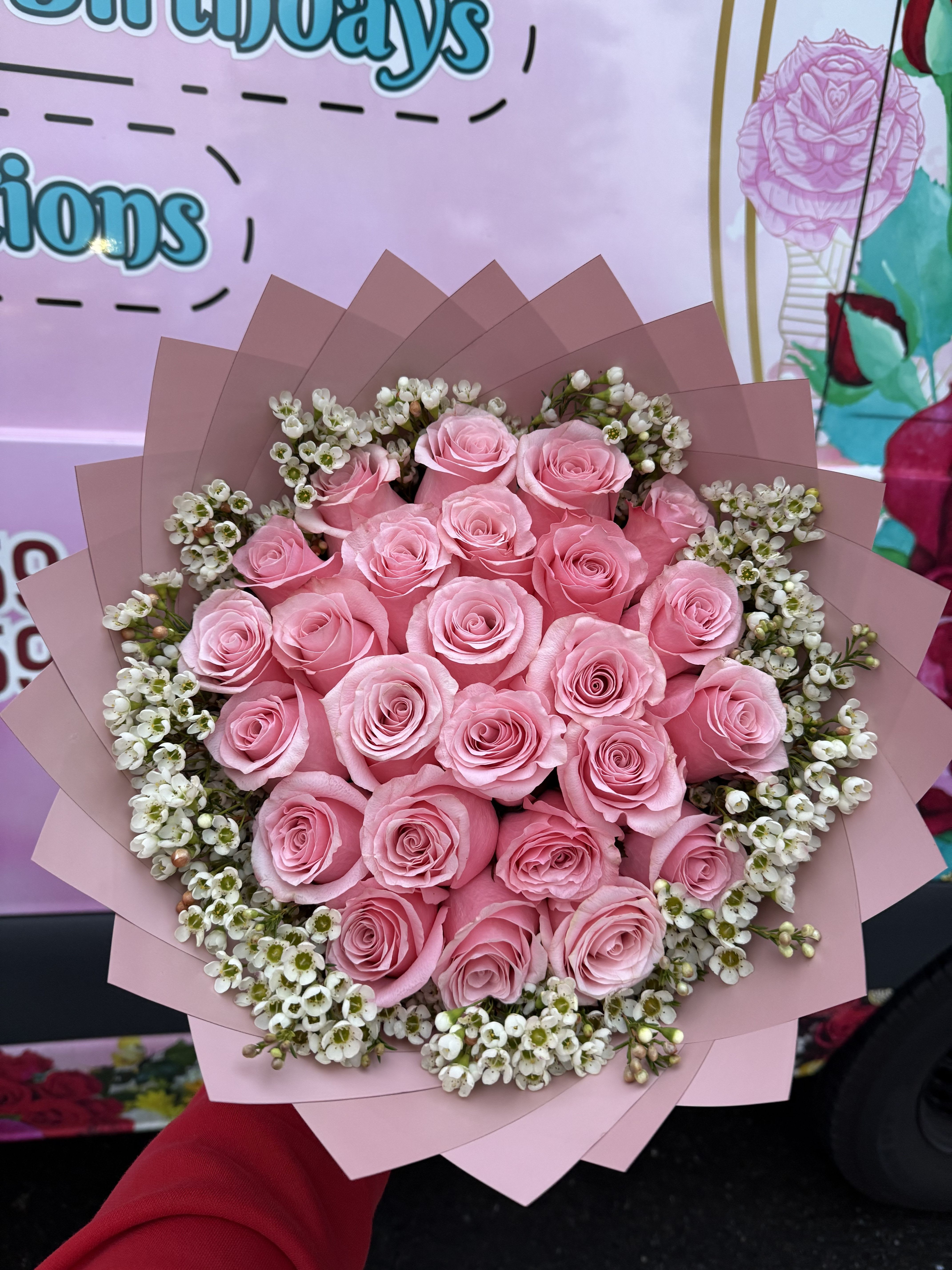 Bouquet of pink roses with small white filler flowers wrapped in pink paper