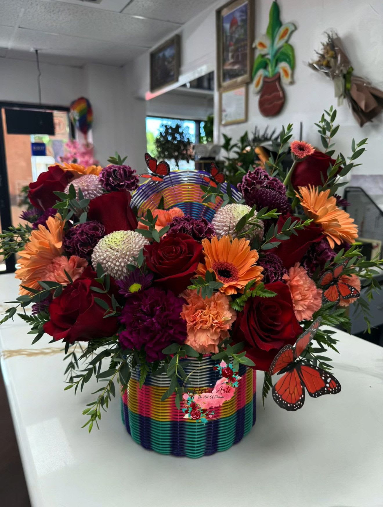 Colorful mixed flower arrangement in a rainbow basket with butterfly picks