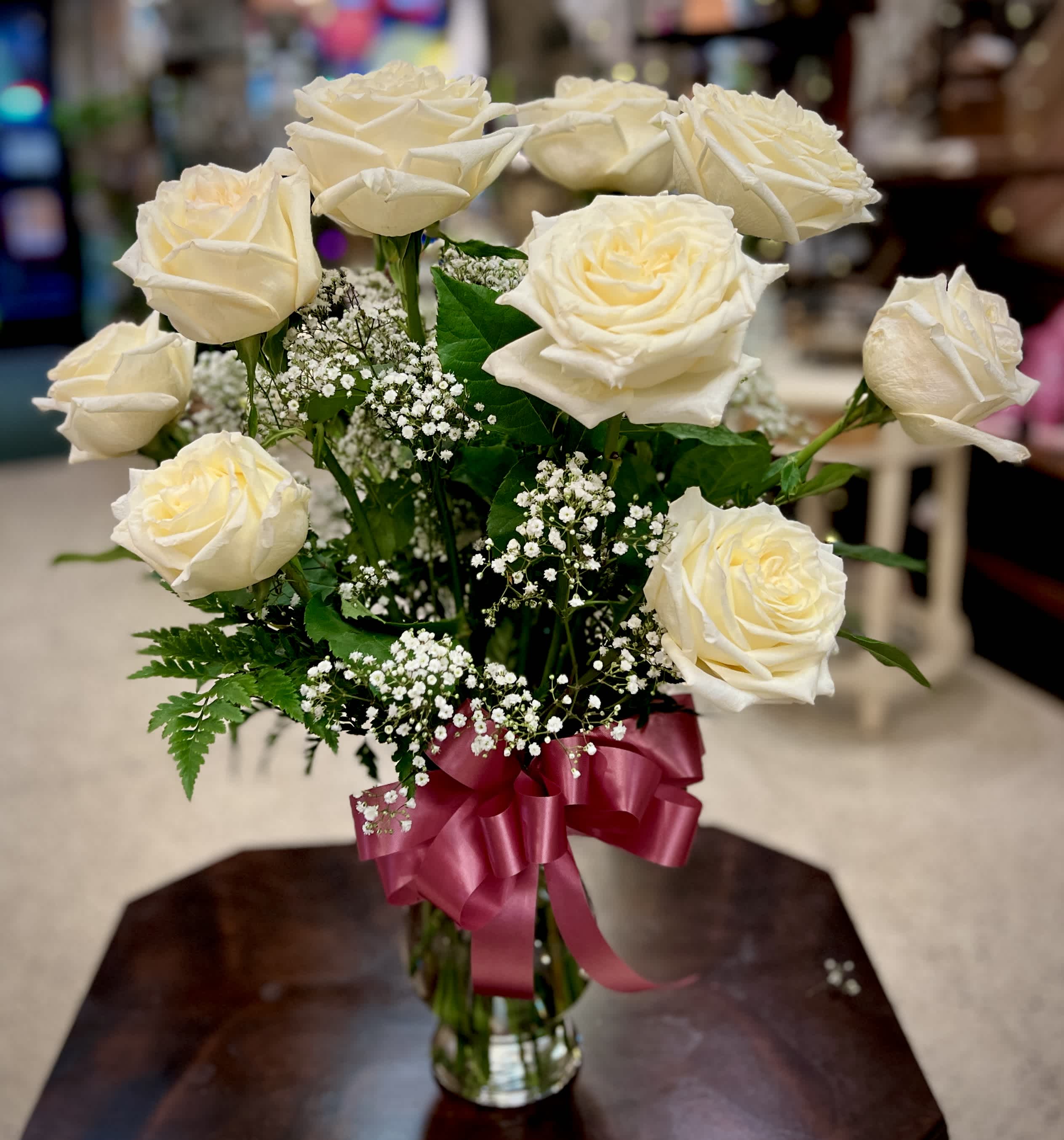 Cream roses in a glass vase with baby's breath and a pink ribbon