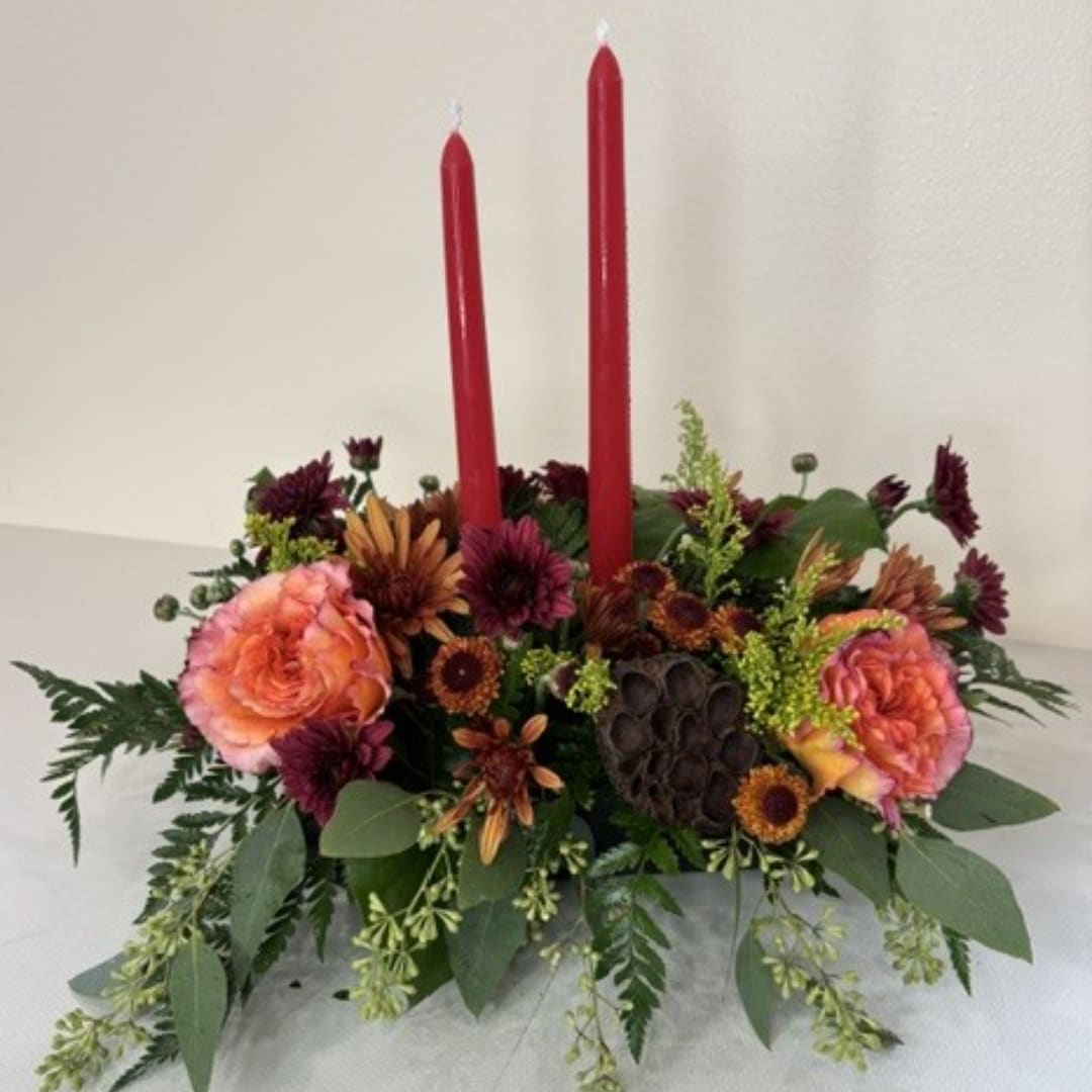 Low floral centerpiece with two red taper candles and peach-orange blooms