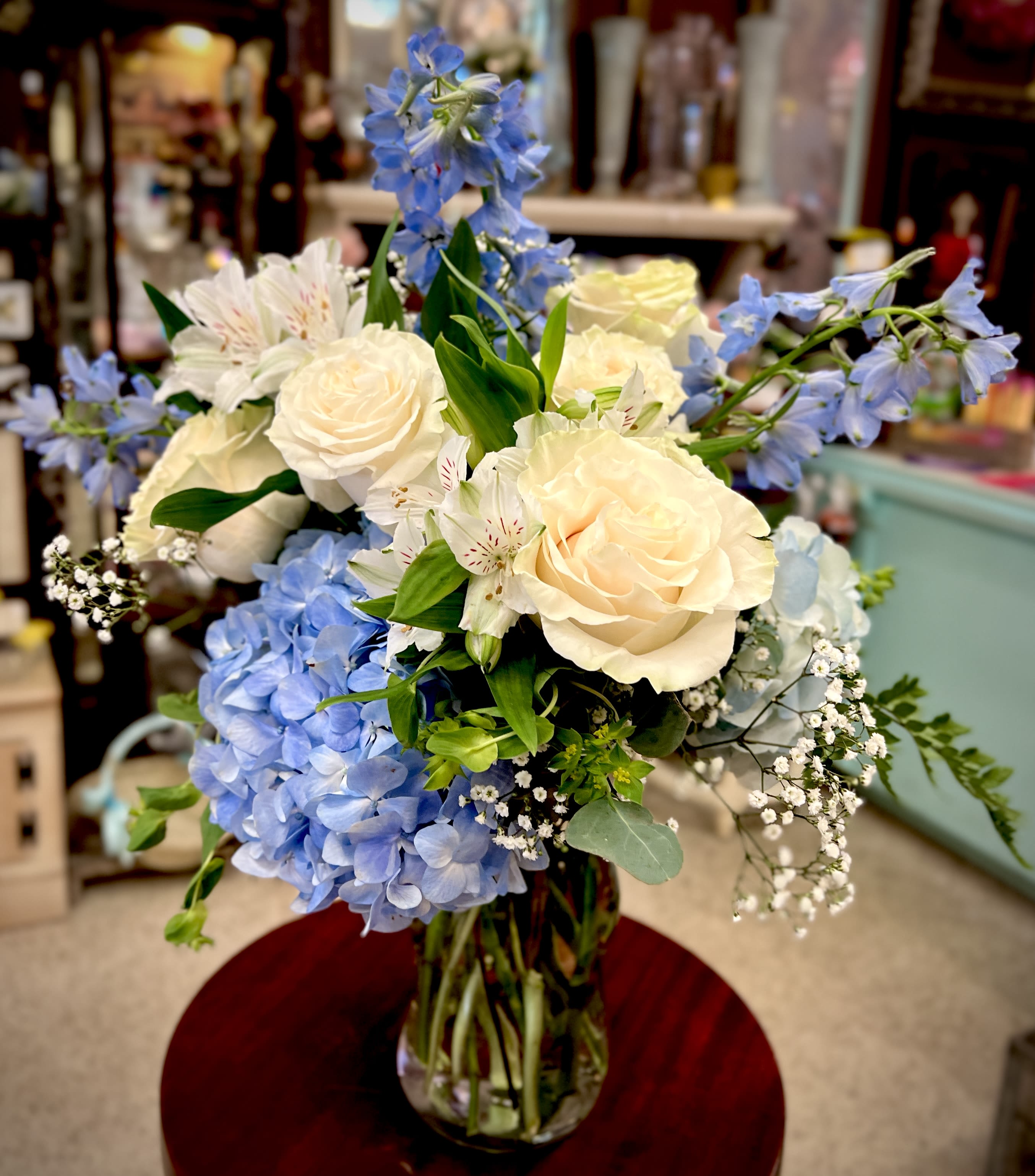 Bouquet of cream roses, blue hydrangeas, and white flowers in a glass vase