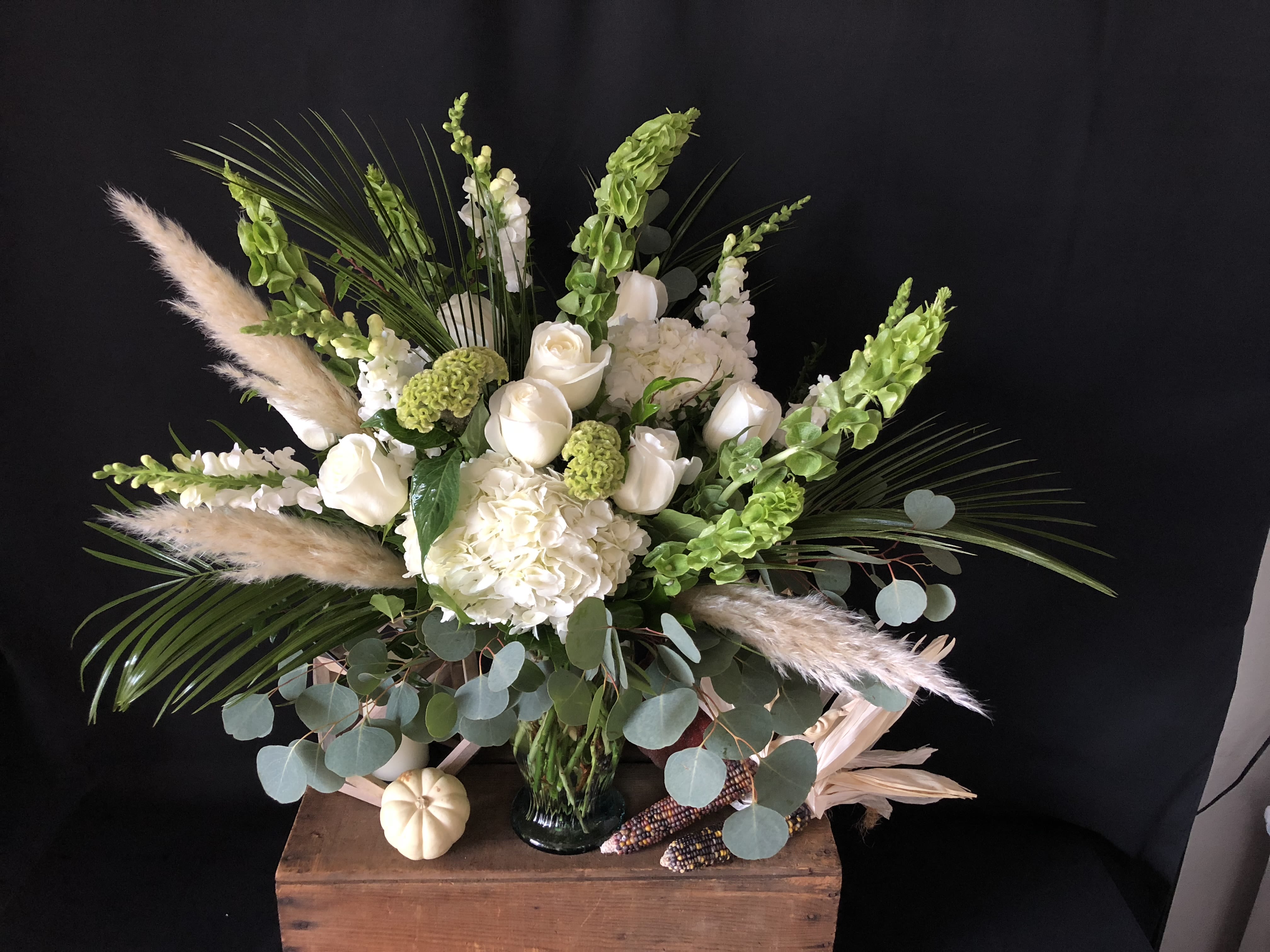 White floral arrangement in a glass vase with green accents and pampas grass