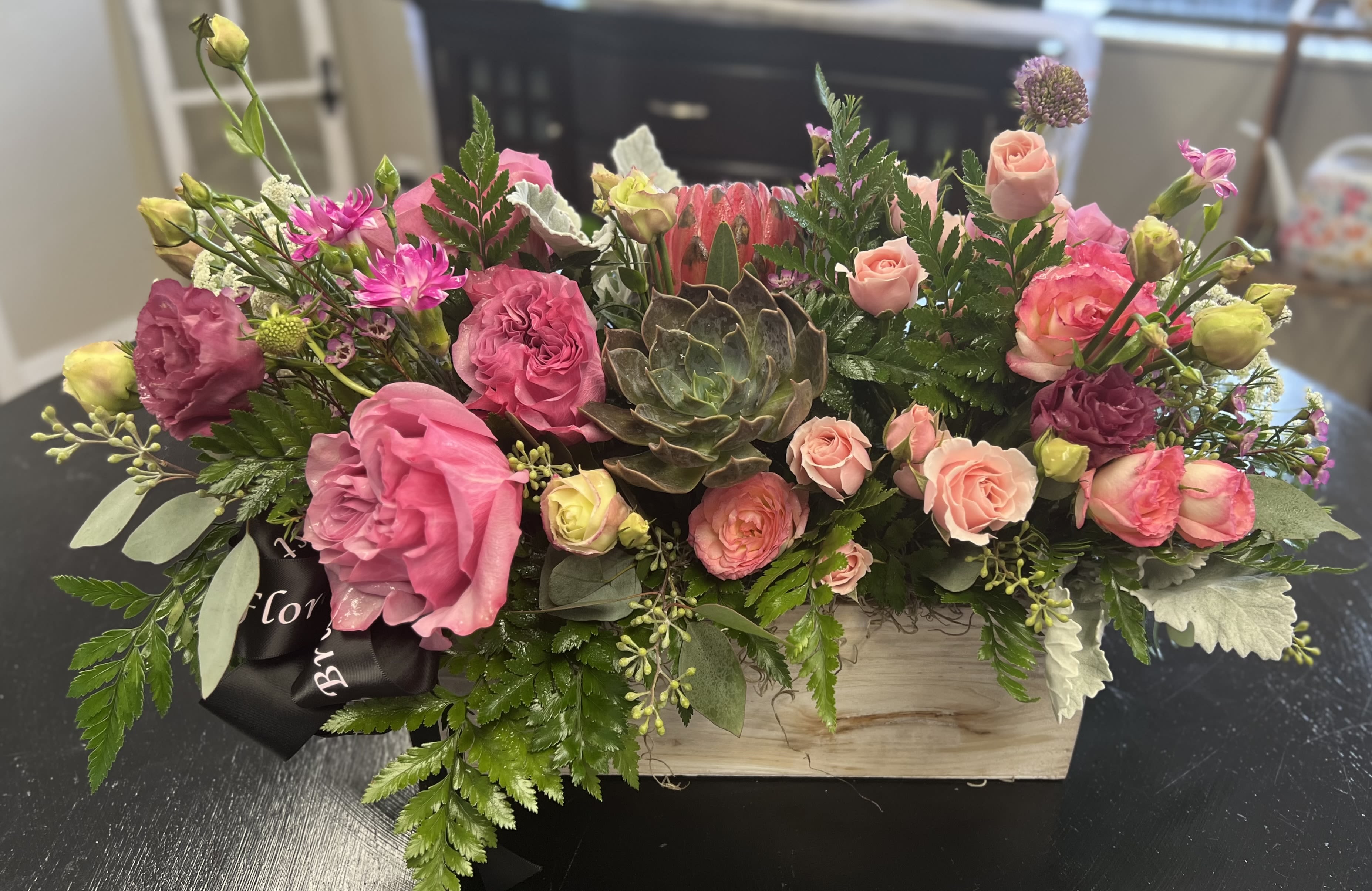 Pink and peach floral arrangement in a wooden box with a succulent center