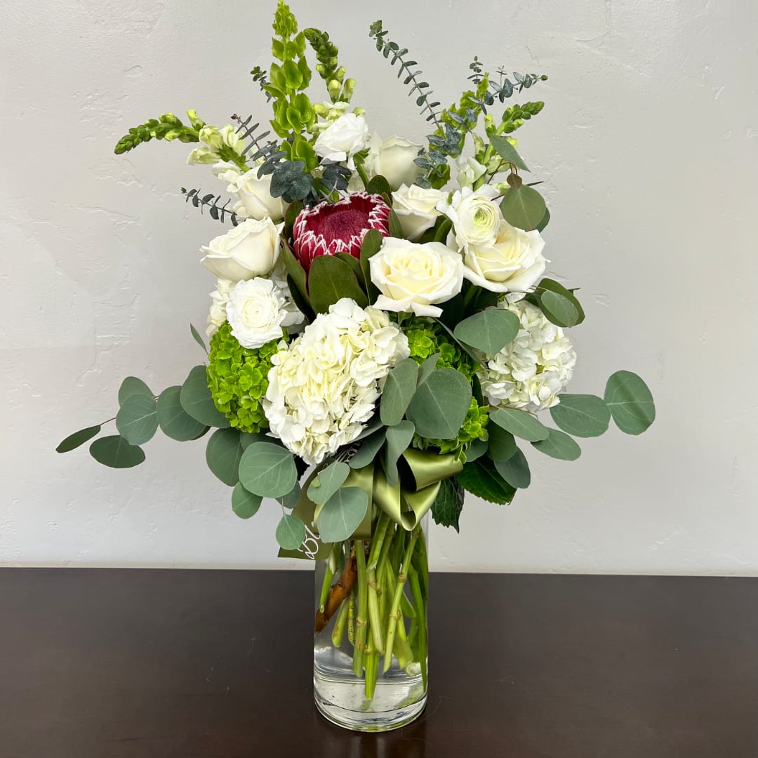 White roses and hydrangeas with green accents in a clear glass vase