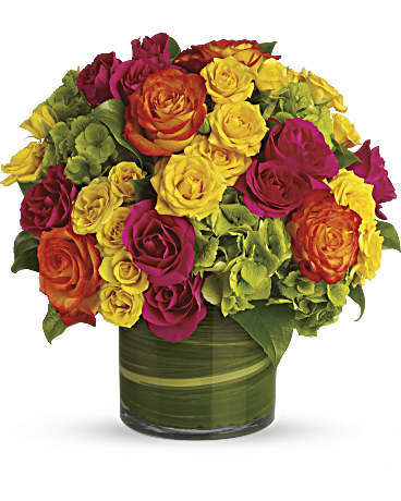 Fall Vogue - High-fashion flowers for the style-minded! This modern presentation of multicolored roses and green hydrangea has a tropical feel thanks to the hot color palette and the aspidistra leaves in the vase. Bright green hydrangea and rich green salal leaves mix with hot pink, yellow, and orange bi-color roses in a clear glass cylinder that's lined with variegated aspidistra leaves. Orientation: All-Around