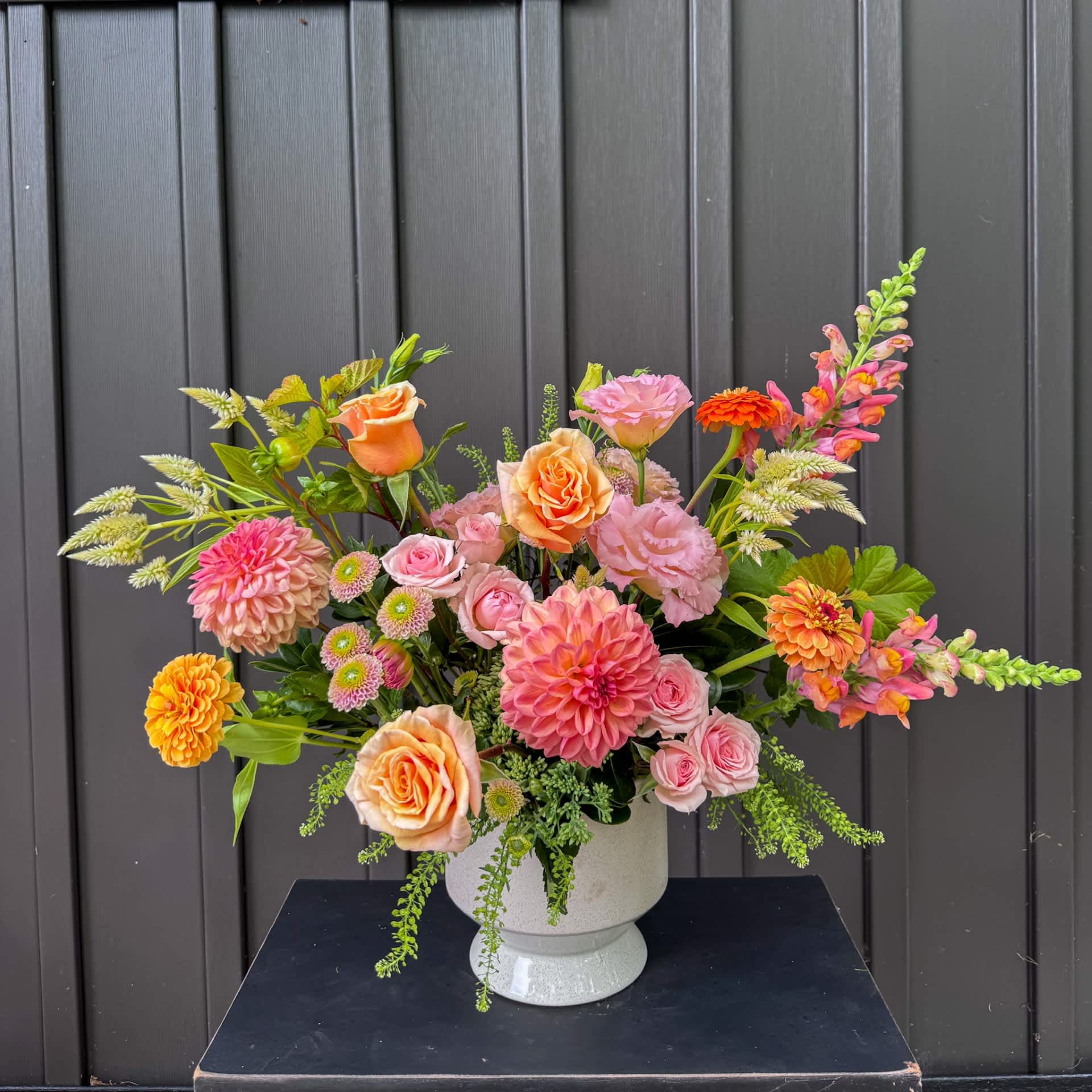 Mixed bouquet of pink, peach, and orange flowers in a white vase