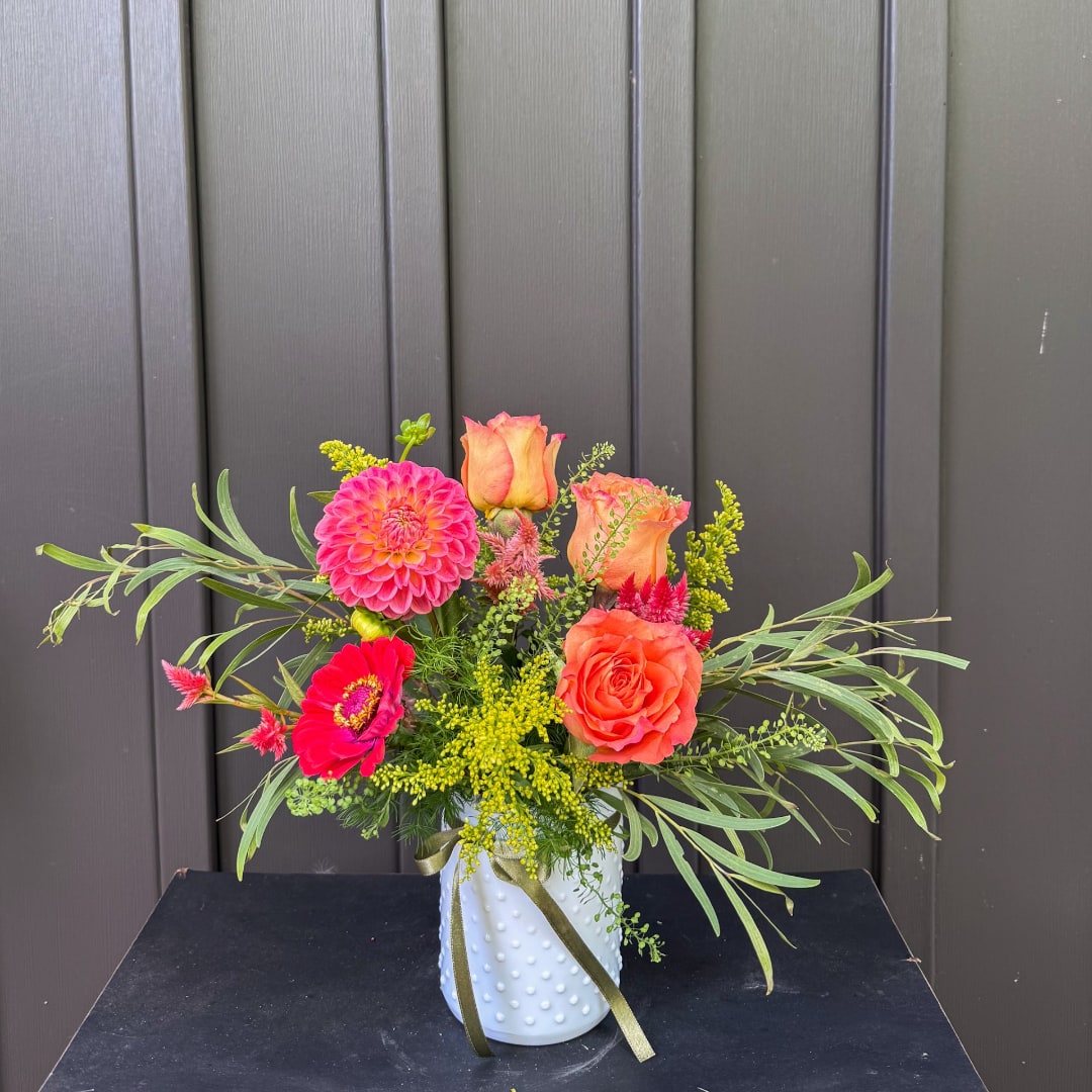 Bright mixed bouquet in a white textured vase with roses and dahlias