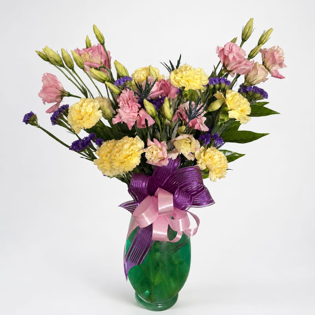 Pink and yellow mixed bouquet in a green glass vase with purple ribbon