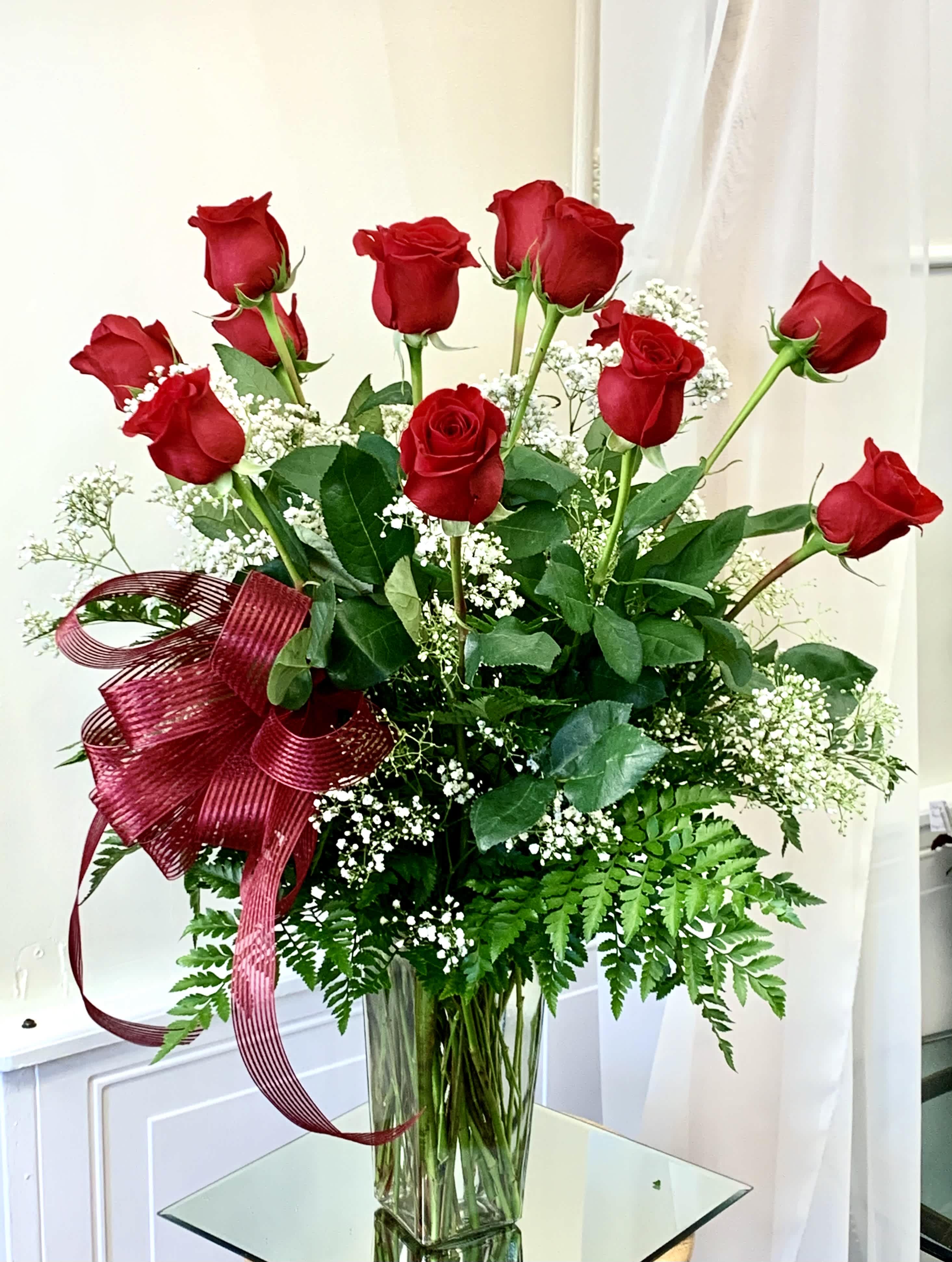 Red roses in a clear glass vase with white baby's breath and a burgundy ribbon