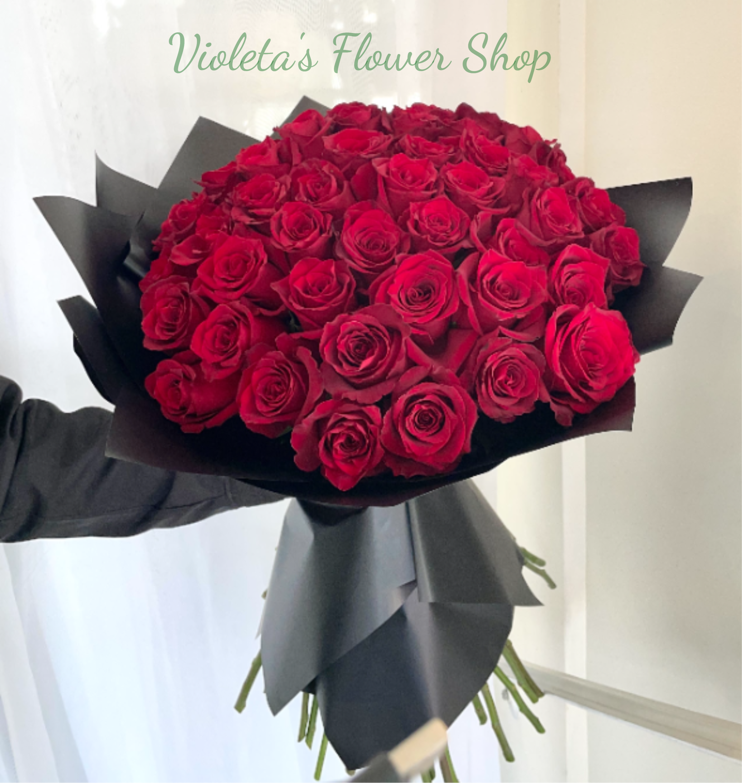 50 Explorer Roses - The long-stemmed roses are gathered tight to form a dense, hand-held bouquet and finished in a matte black paper wrap that heightens contrast and gives a contemporary, formal edge. The rich, velvety red petals and the stark black wrapping make a striking color statement perfect for someone who appreciates bold elegance.  Ideal for marking milestone moments or saying "I love you" in a way that feels unforgettable, this arrangement arrives ready to present-no extra fussy handling required. To keep the roses looking their best, place them in fresh water and trim stems slightly; their large size and dramatic presentation make them a standout centerpiece as well as a personal gift.