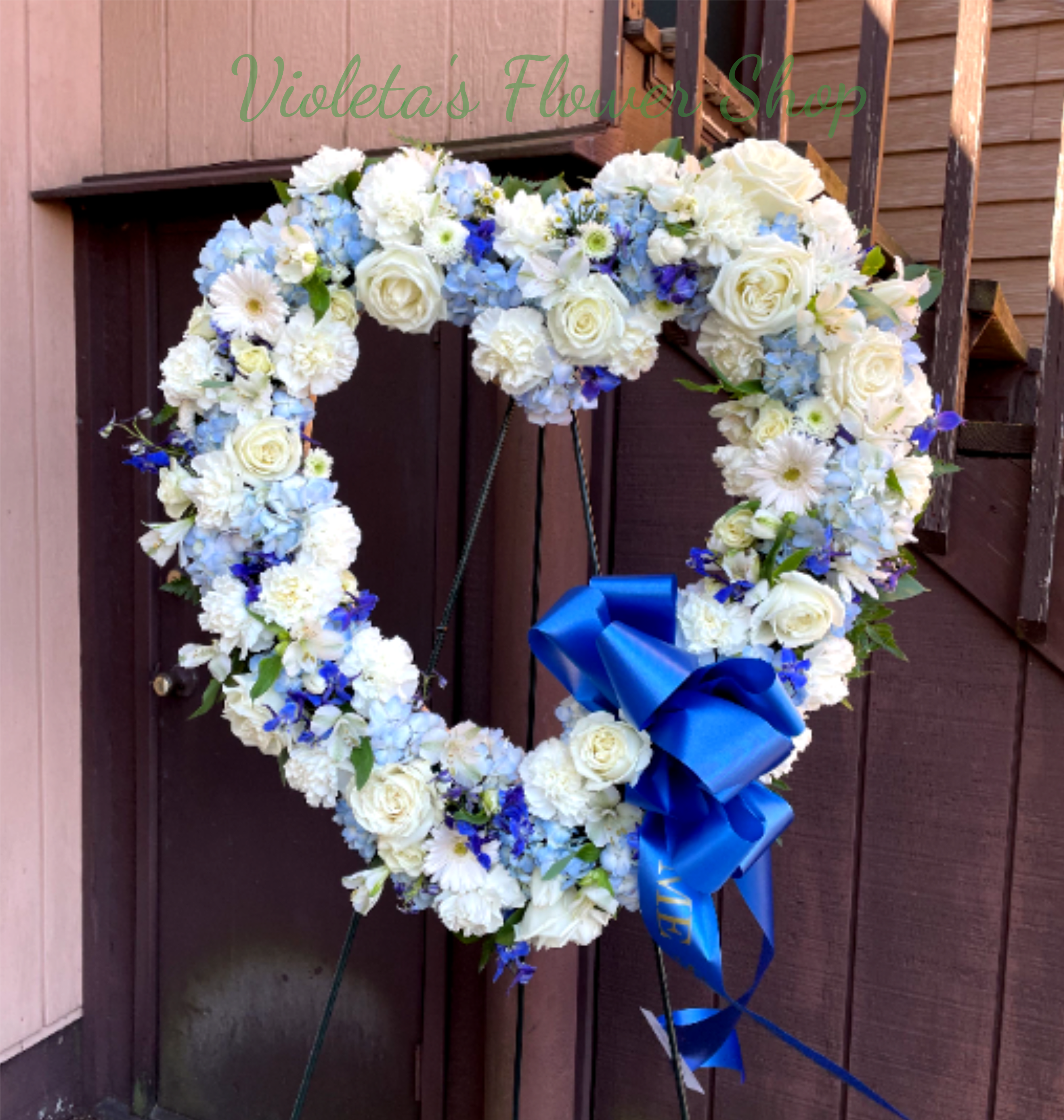 Heart-shaped floral wreath with white and blue flowers and a blue ribbon bow