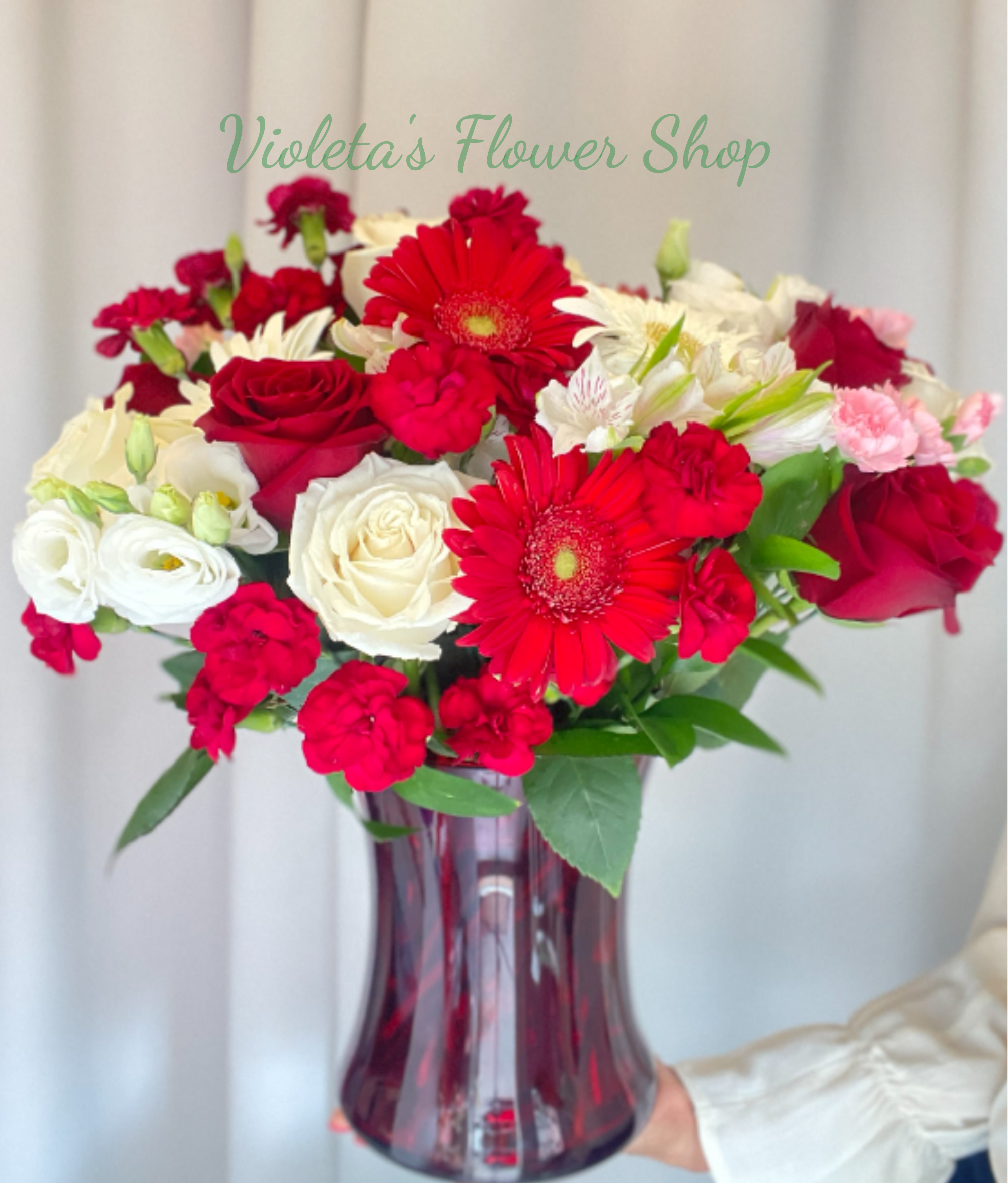 Forever Yours - Bright, romantic and unmistakable - this Forever Yours flower arrangement is a birthday bouquet or anniversary gift that reads like a declaration. Large red gerbera daisies and red roses command the eye, while white roses and white alstroemeria bring luminous contrast and small pink carnations add soft texture; the mix of red, white, pink, and green creates a lively, celebratory palette perfect for love, Valentine's Day, or marking a special milestone.  Arranged densely in a tall glass vase (flared and red in one styling), the composition is upright and full, making it feel like a substantial centerpiece as soon as it arrives. Expect layered depth from the varied bloom sizes - bold gerberas, classic roses, delicate alstroemeria and ruffled carnations - presented gift-ready for the person you're celebrating. 