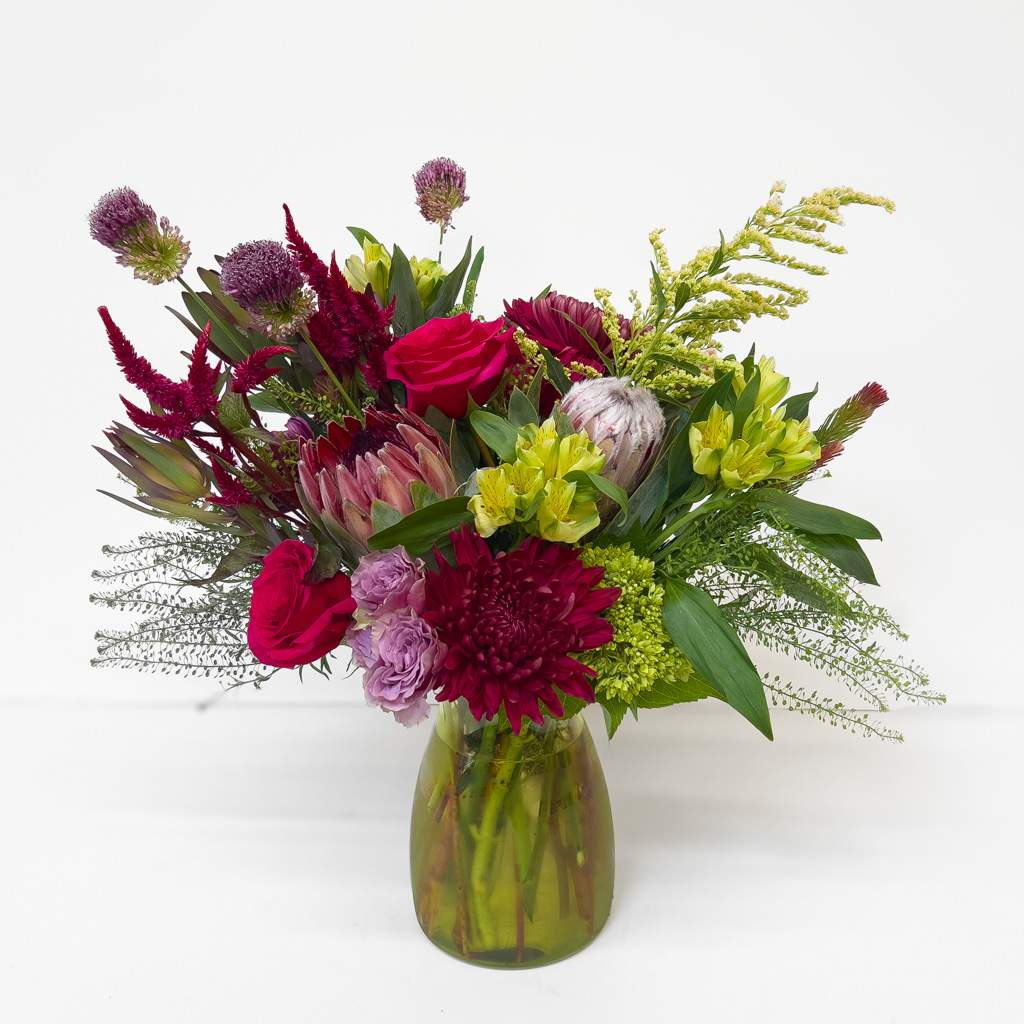 Mixed bouquet of magenta, purple, and yellow flowers in a glass vase