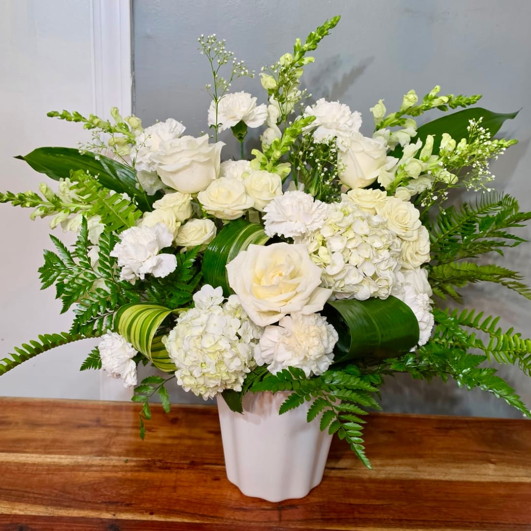 White floral arrangement in a white vase with green foliage