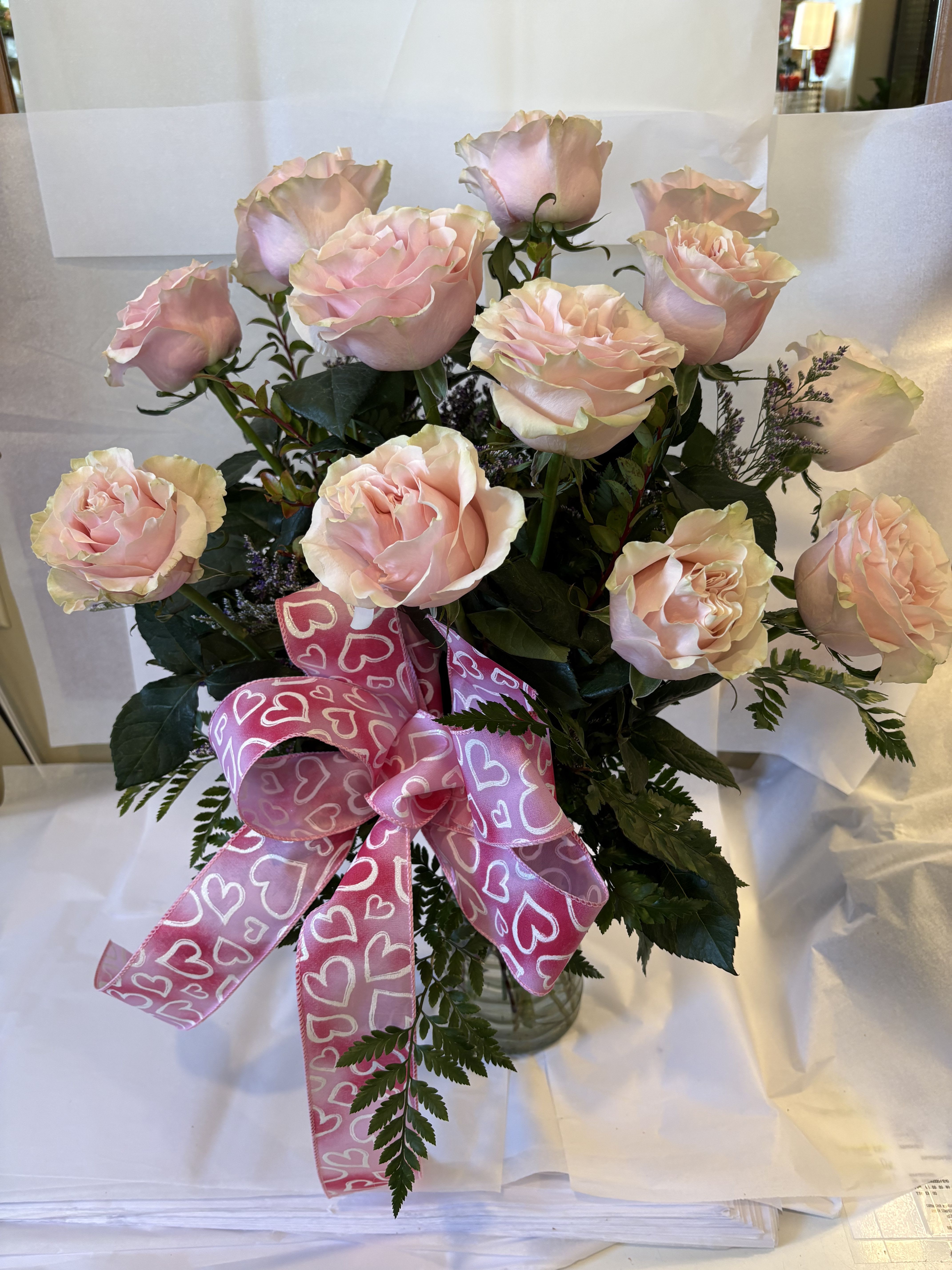 Bouquet of pale pink roses with a pink heart ribbon in a glass vase