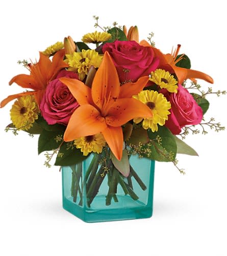 Bright orange lilies, pink roses, and yellow blooms in a turquoise glass cube vase