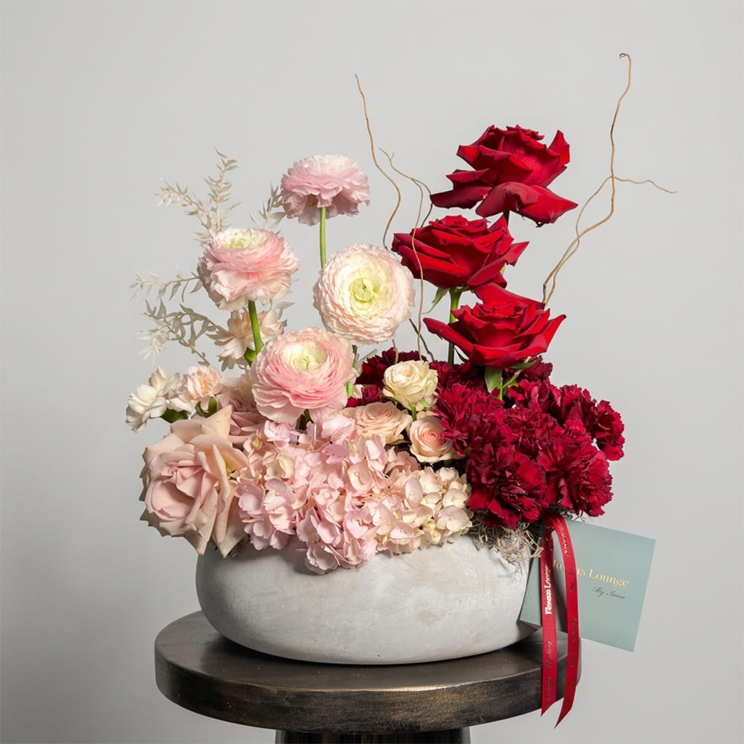 Mixed floral arrangement in a white bowl with red and blush blooms