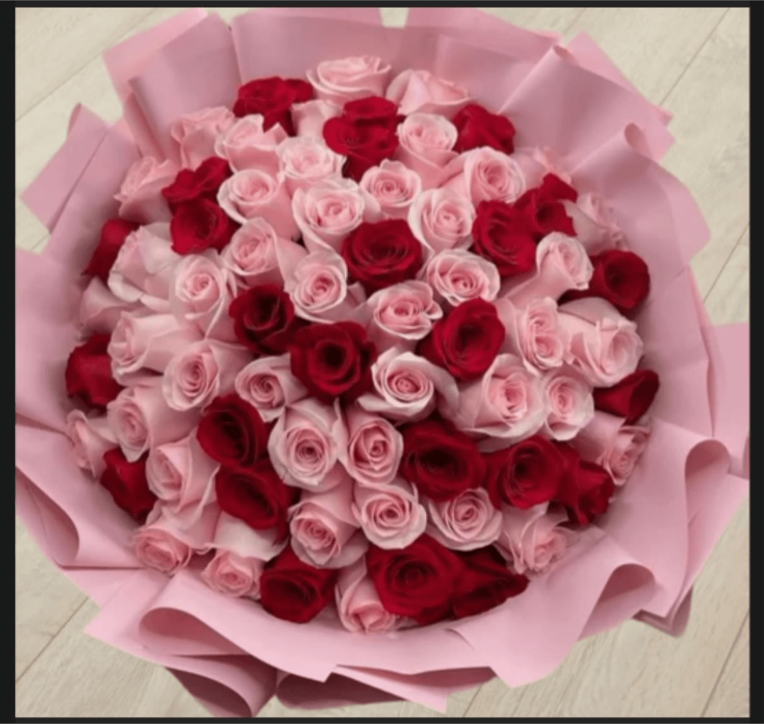 MICAELA PINK AND RED ROSES - A lush dome of tightly packed roses in alternating blush pink and deep red makes an unforgettable romantic bouquet for anniversaries, Valentine's Day, or any occasion when you want the person you're thinking of to feel adored. The hand-tied arrangement reads as both classic and celebratory - the high-contrast pairing of soft pink and passionate red instantly signals love and devotion while the dense, rounded shape feels opulent and intentional.  Every bloom is a rose, arranged in a full, rounded composition that emphasizes color rhythm and texture. The bouquet is finished in soft pink wrapping paper that frames the flowers with a gentle pastel edge, enhancing the blush tones and making the reds pop. Presented hand-tied for easy holding and gifting, it has a generous, full silhouette that reads large and luxurious.  Perfect for the partner who deserves something striking and heartfelt, this bouquet says "you are cherished" without words. Order with confidence for delivery on special dates or just-because moments; minimal care is required-keep blooms in fresh water and away from direct heat to prolong their beauty.