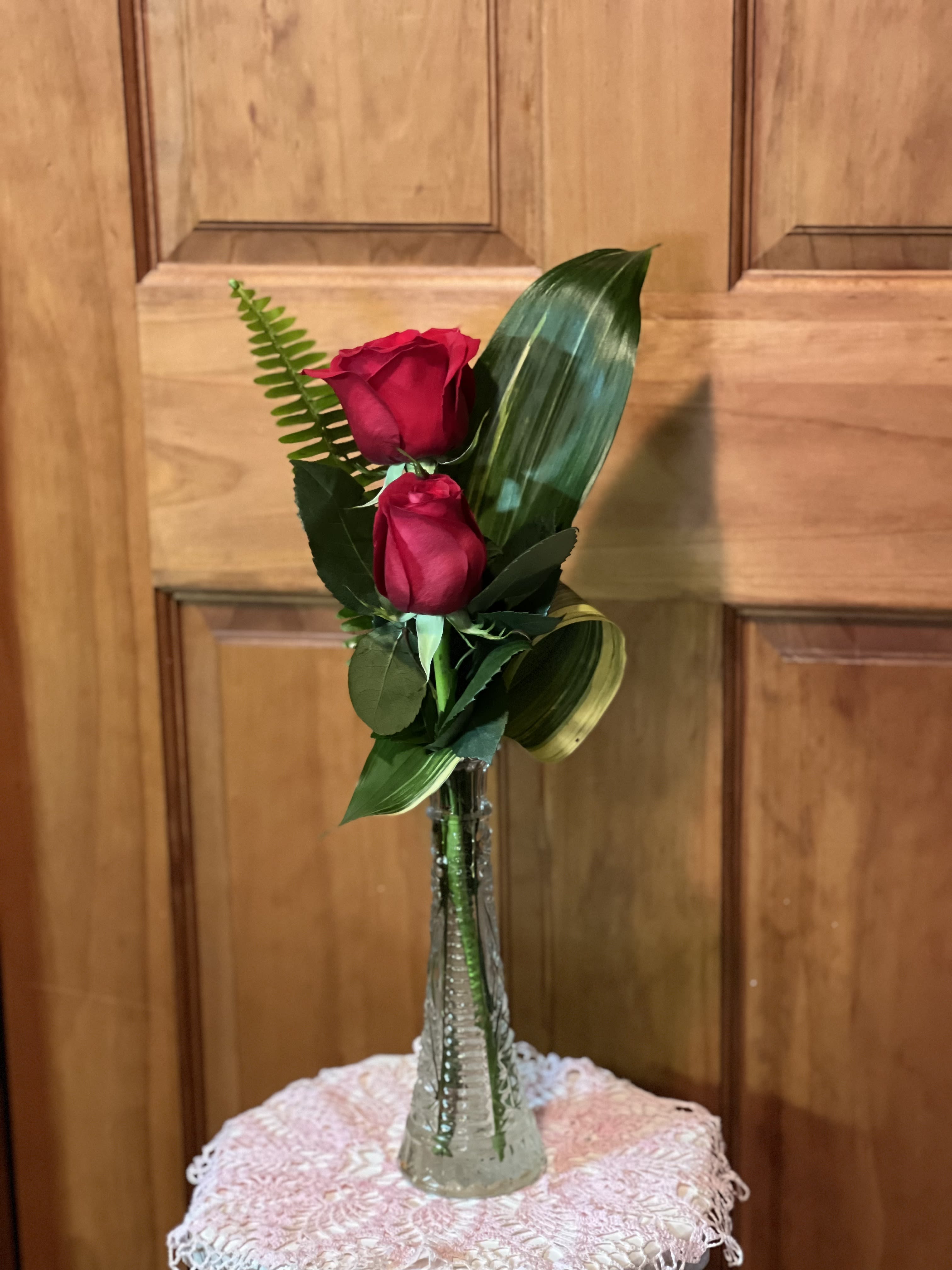 Two red roses in a clear glass vase with assorted greenery