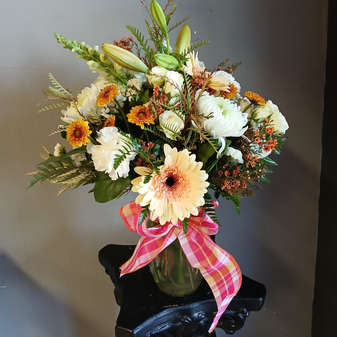 Mixed bouquet of white and peach flowers in a glass vase with a pink plaid ribbon