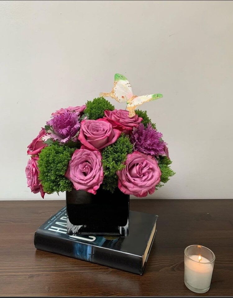 Pink roses in a black vase with a small butterfly topper